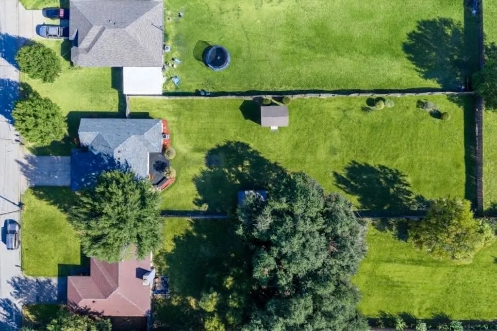 Expansive lot with lush green lawn, mature trees, paved driveway, and detached storage shed