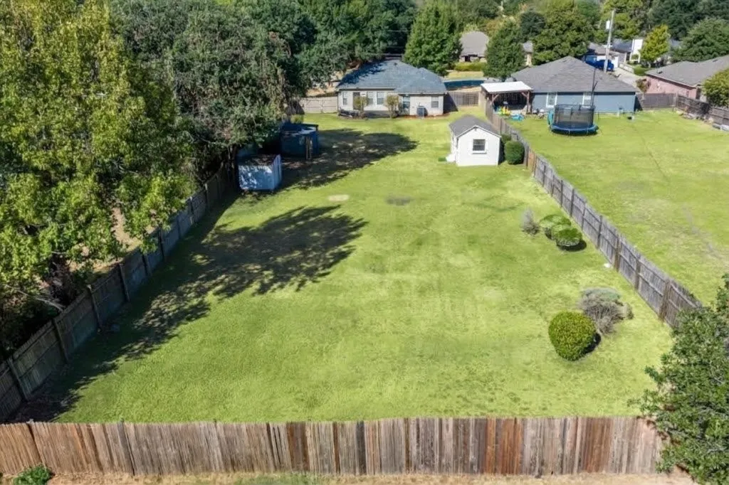 Expansive fenced yard featuring a storage shed and mature trees