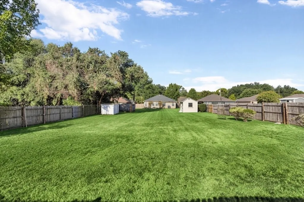 Expansive fenced backyard with a lush green lawn, mature trees, and a storage shed