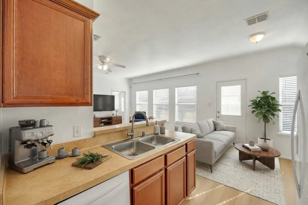 Wood-finish flooring, two-compartment stainless steel sink, wood cabinetry, multiple windows with blinds, and white walls