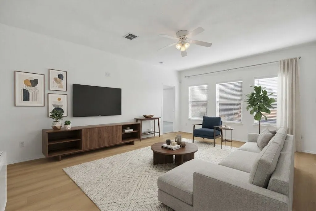 Wood-finish flooring, white walls, multiple windows with blinds, and a ceiling fan with integrated lighting