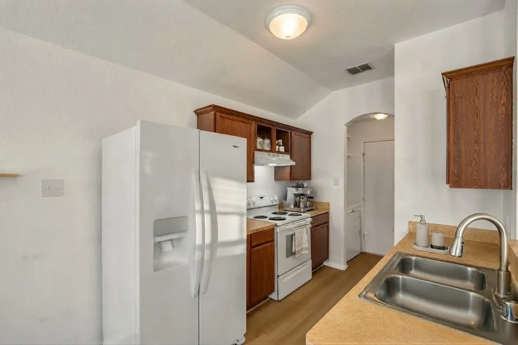 Kitchen featuring wood-finish cabinetry, a double basin stainless steel sink, a range with an overhead exhaust, and a side-by-side refrigerator