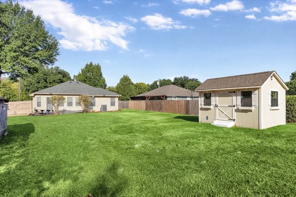 Expansive backyard featuring a manicured lawn, a detached storage shed with a shingled roof, and a privacy fence