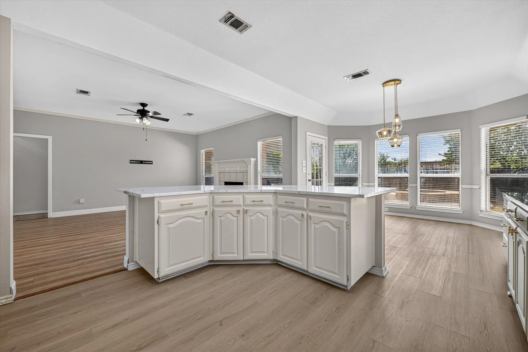 Kitchen island with white cabinetry and light-toned countertop, wood-finish flooring, recessed lighting, and a multi-pendant light fixture