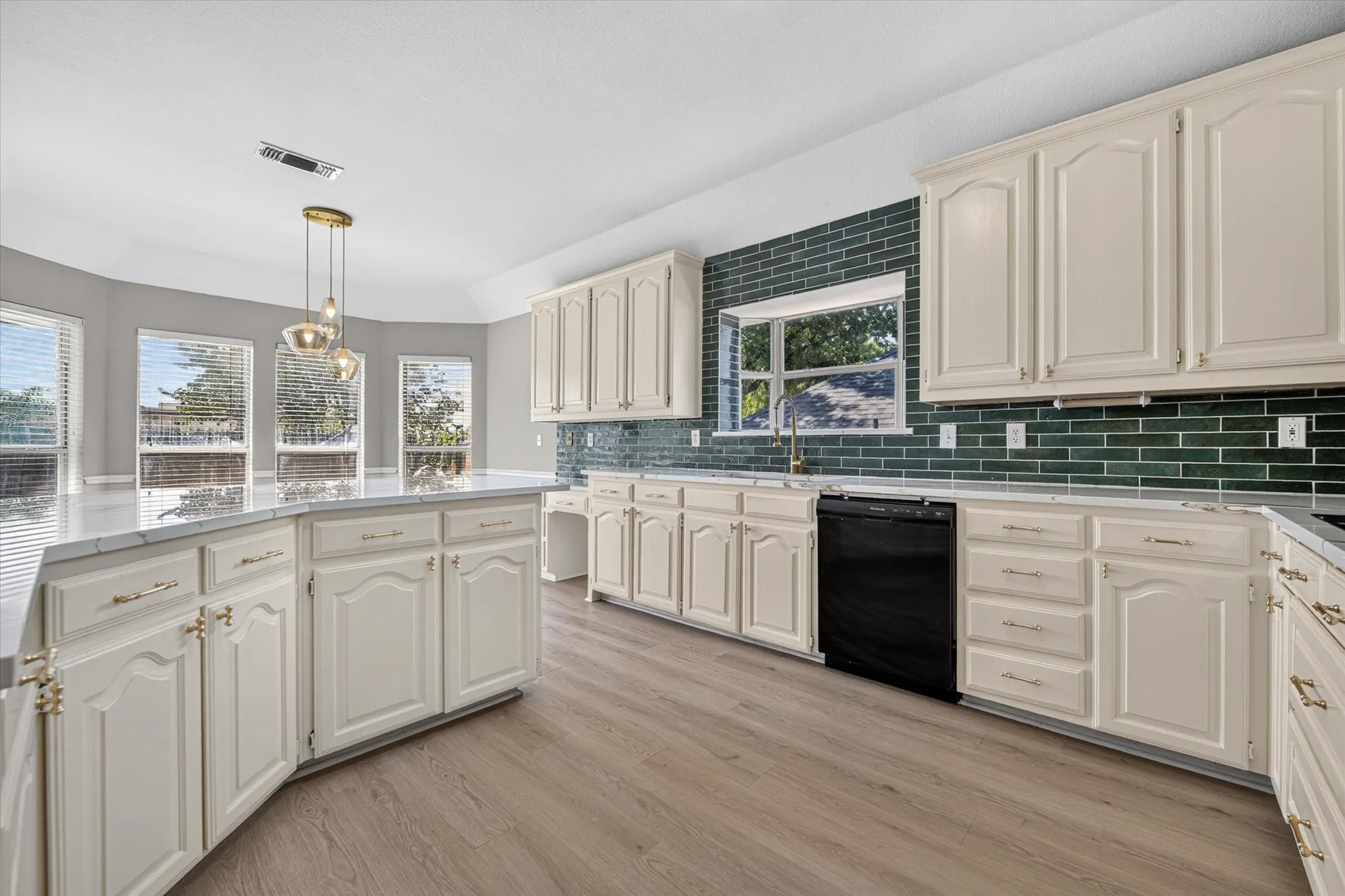 Kitchen featuring light cabinetry, dark green subway tile backsplash, light wood-finish flooring, and a central island with a pendant light fixture