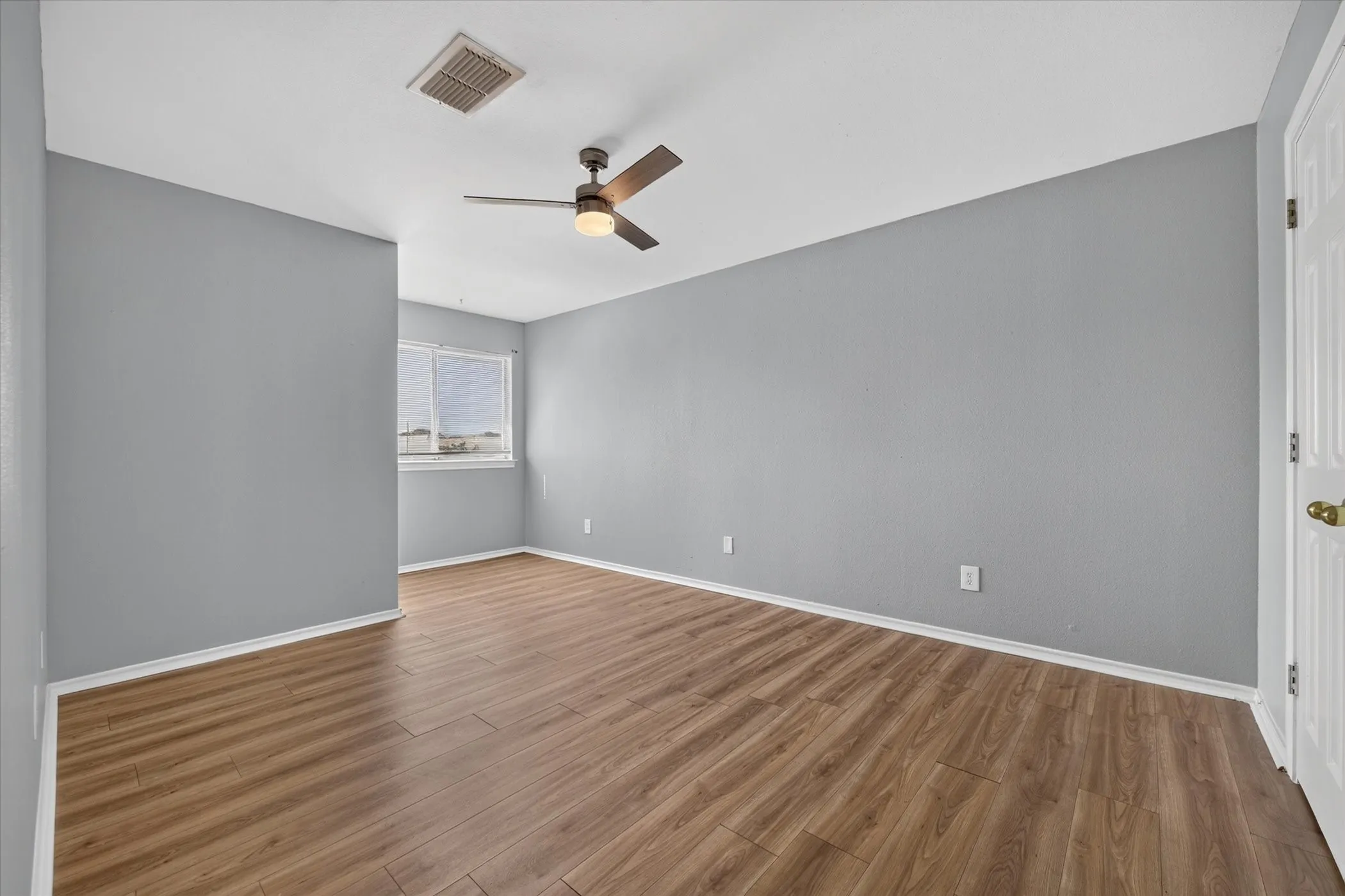 Wood-finish flooring, neutral gray walls, and a ceiling fan with integrated lighting