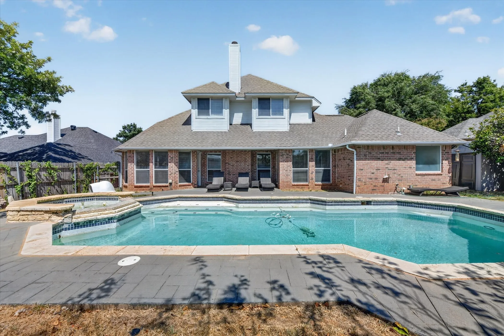 Brick exterior with dormer windows, a pitched shingle roof, a rectangular swimming pool, and an attached spa with stone coping