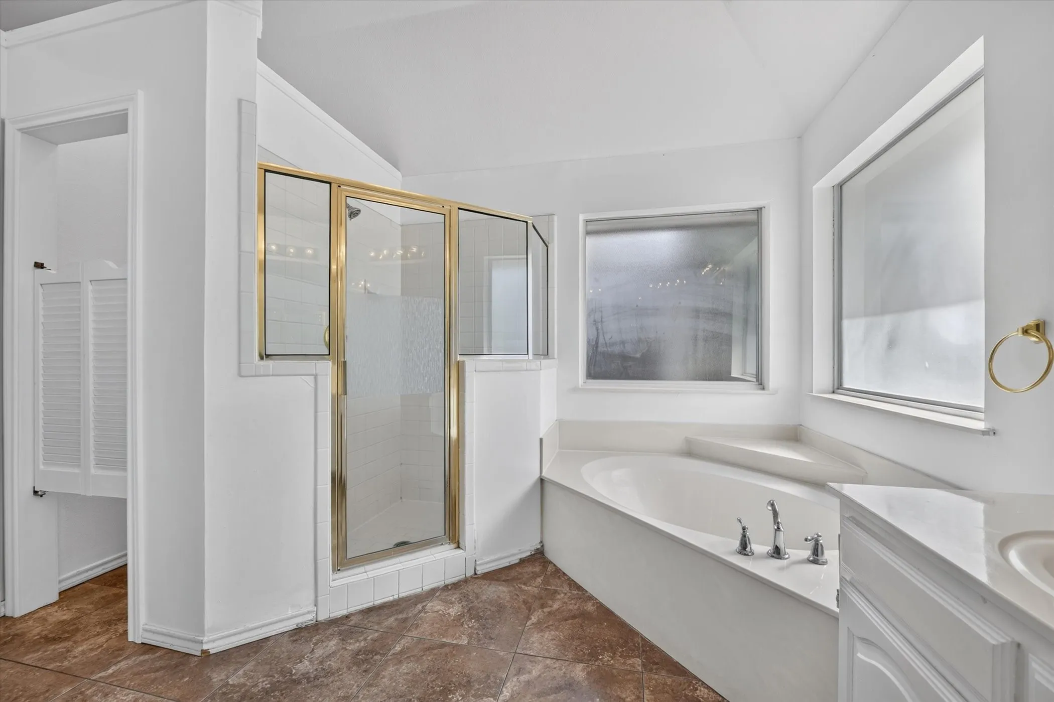Corner soaking tub, separate shower with glass enclosure, dual vanity, and frosted windows