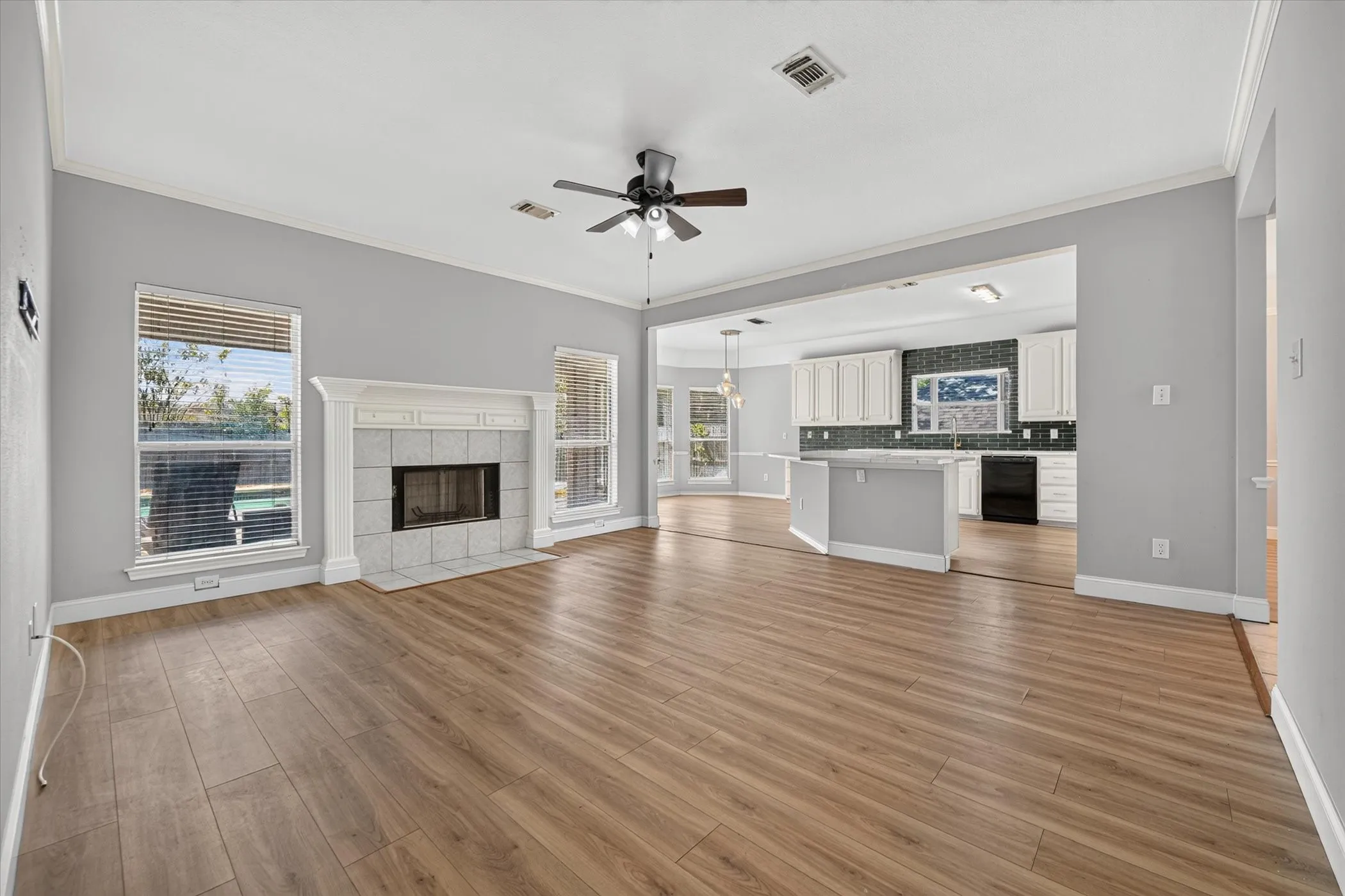 Wood-finish flooring throughout, vaulted ceiling, white mantel with a tile-surround fireplace, and an open concept layout with an expansive kitchen
