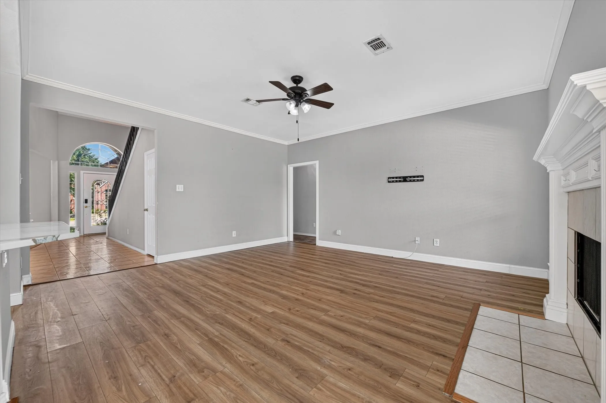 Spacious living area featuring wood-finish flooring, a ceiling fan, and a fireplace with a decorative mantel and tiled hearth