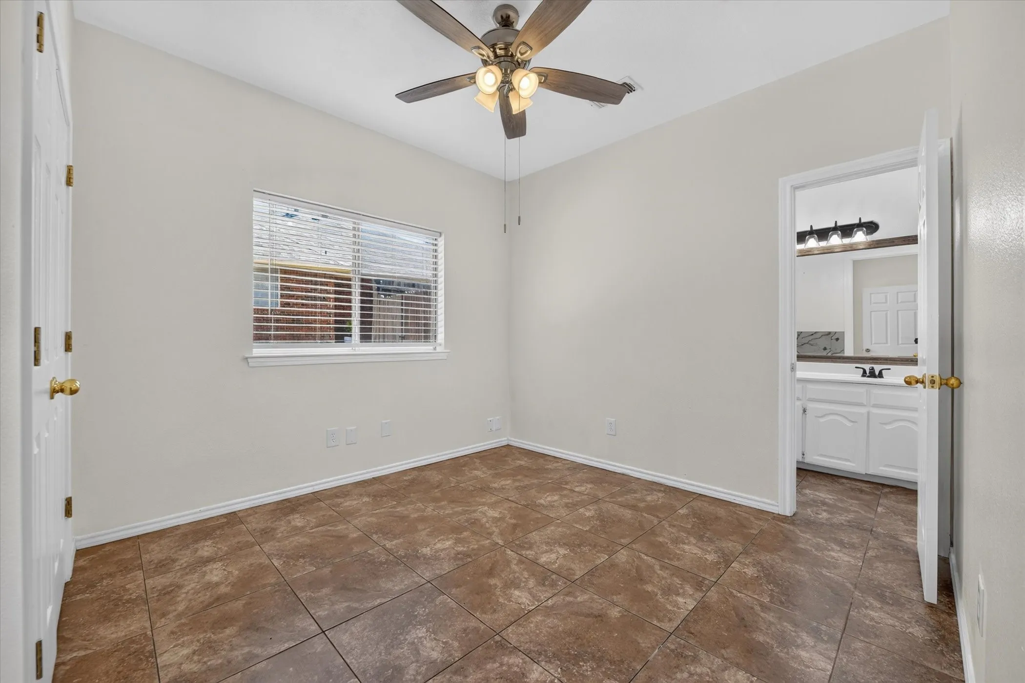 Neutral wall paint, ceiling fan with integrated lighting, window with blinds, tile flooring, and an en-suite bathroom with a vanity