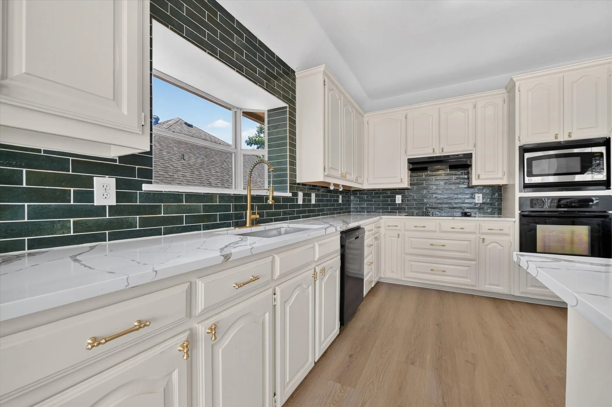Kitchen featuring white cabinetry, light countertops, dark subway tile backsplash, stainless steel appliances, and light wood-finish flooring