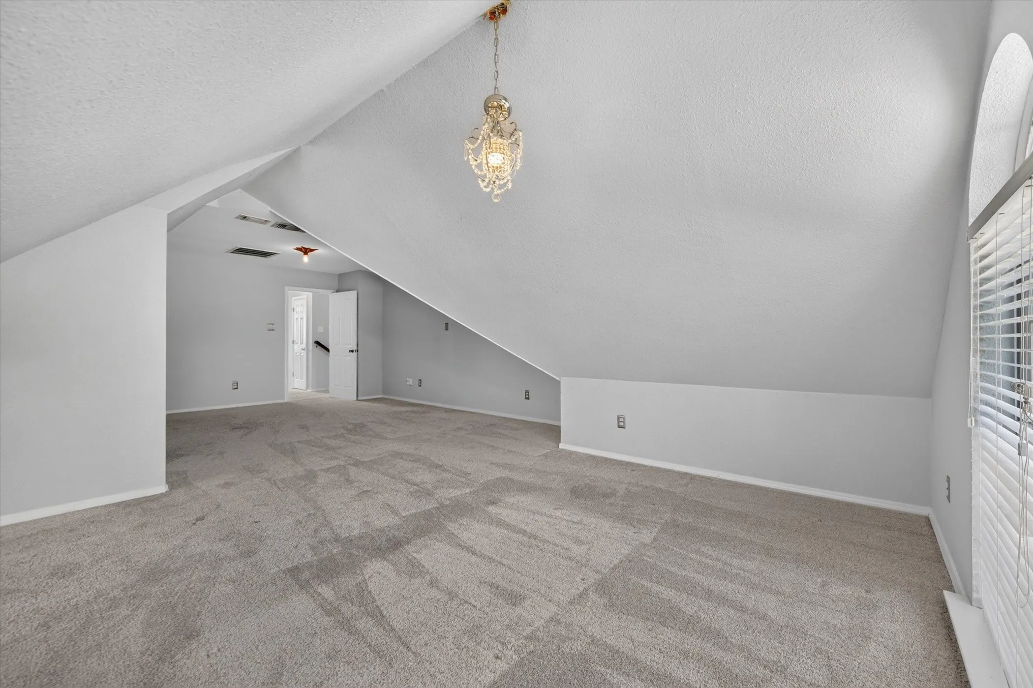 Spacious room featuring vaulted ceilings, neutral-toned carpeting, an arched window, and a decorative pendant light fixture