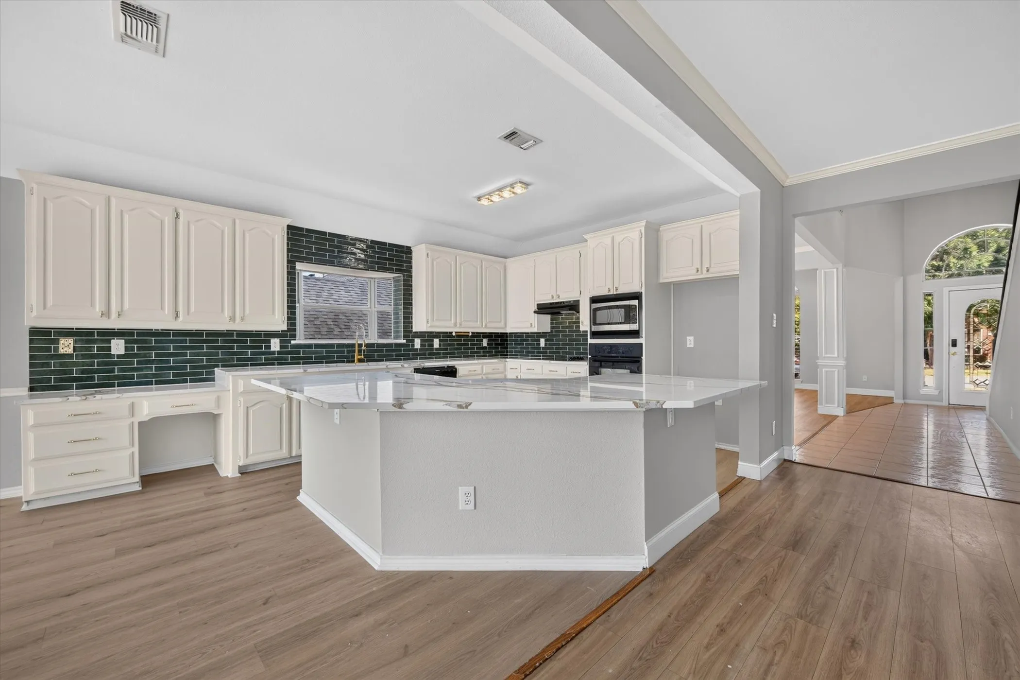 Kitchen featuring a large central island, white cabinetry, integrated stainless steel appliances, and wood-finish flooring