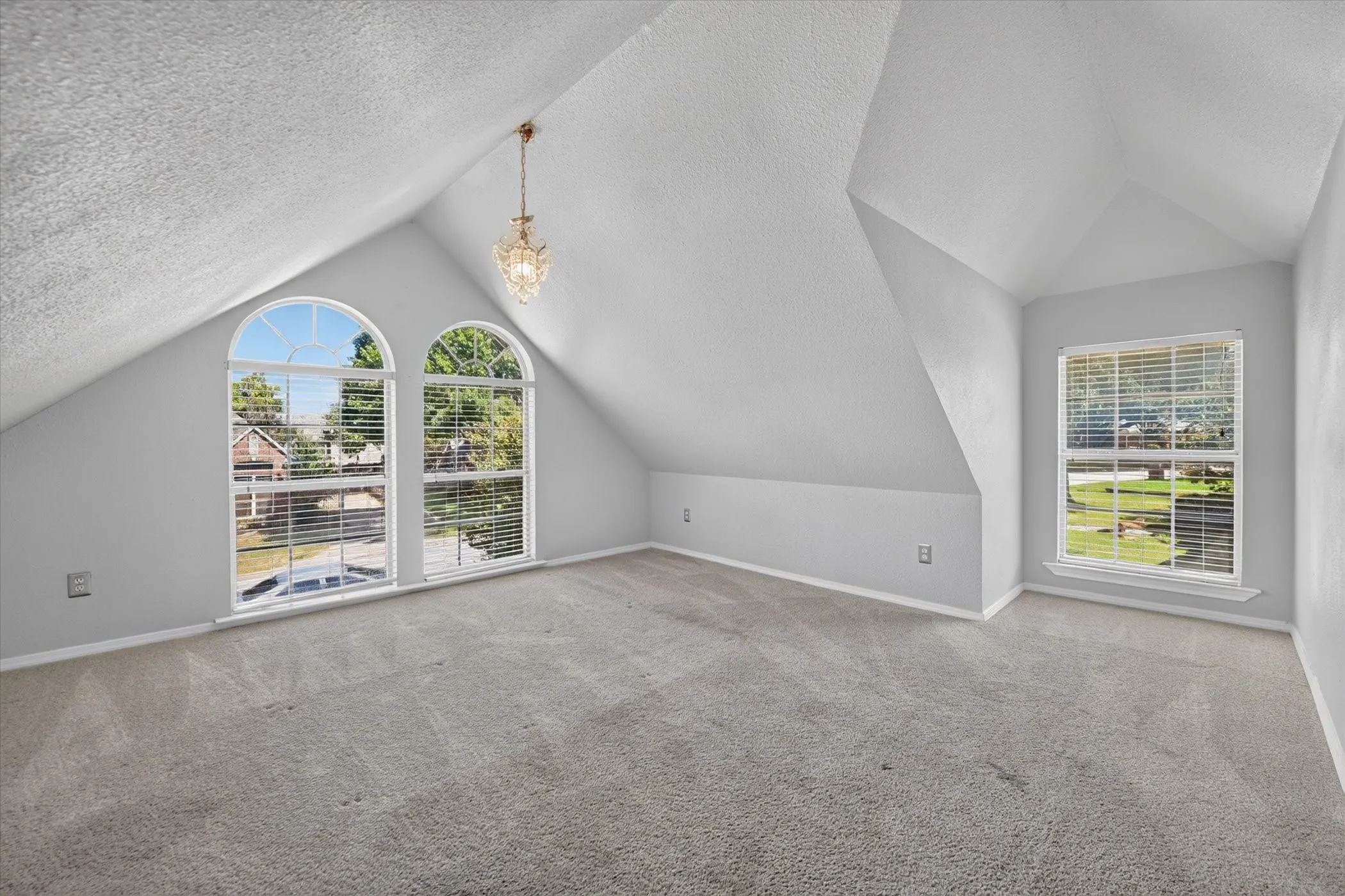 Vaulted ceiling with a central chandelier, arched windows, rectangular window, and carpeted flooring