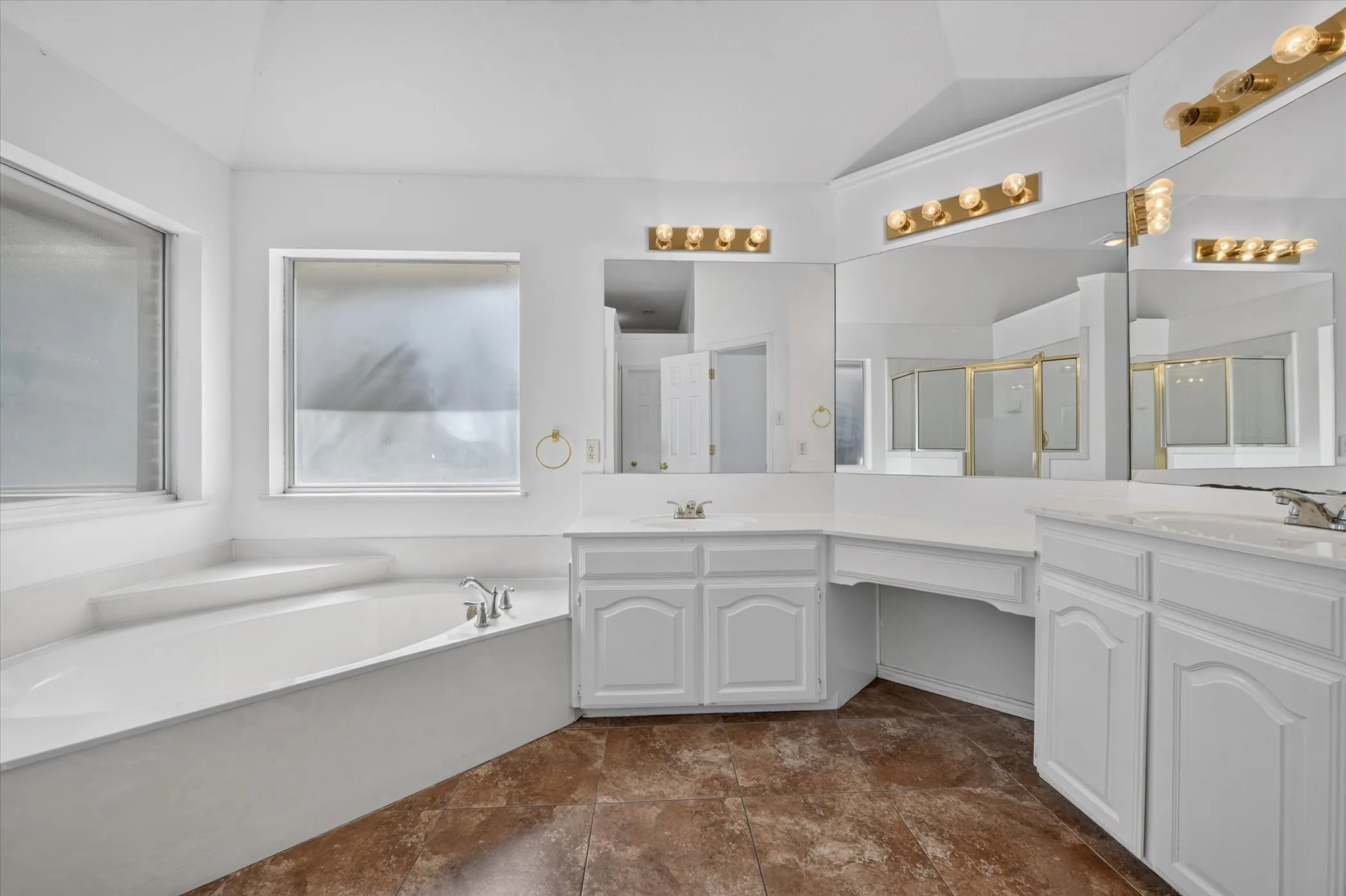 Corner soaking tub, dual vanities with integrated sinks, large wall-mounted mirrors, vanity lighting, and ceramic tile flooring
