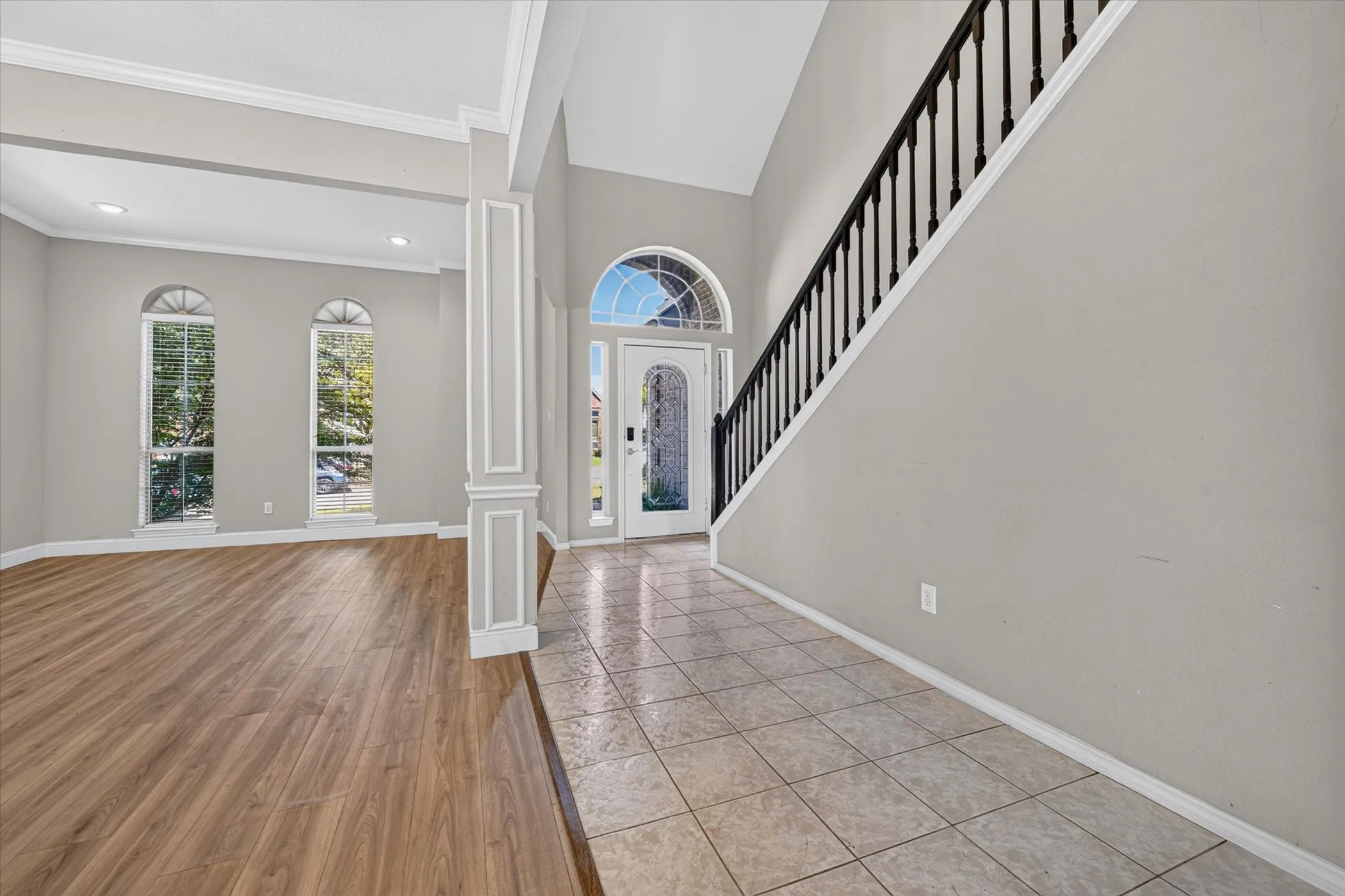Two-story entry with an arched transom door, tile flooring, and a staircase featuring a dark wood-finish handrail
