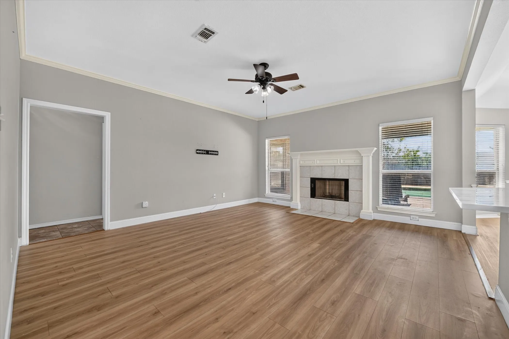 Vaulted ceiling, wood-finish flooring, fireplace with tile surround, ceiling fan, and crown molding