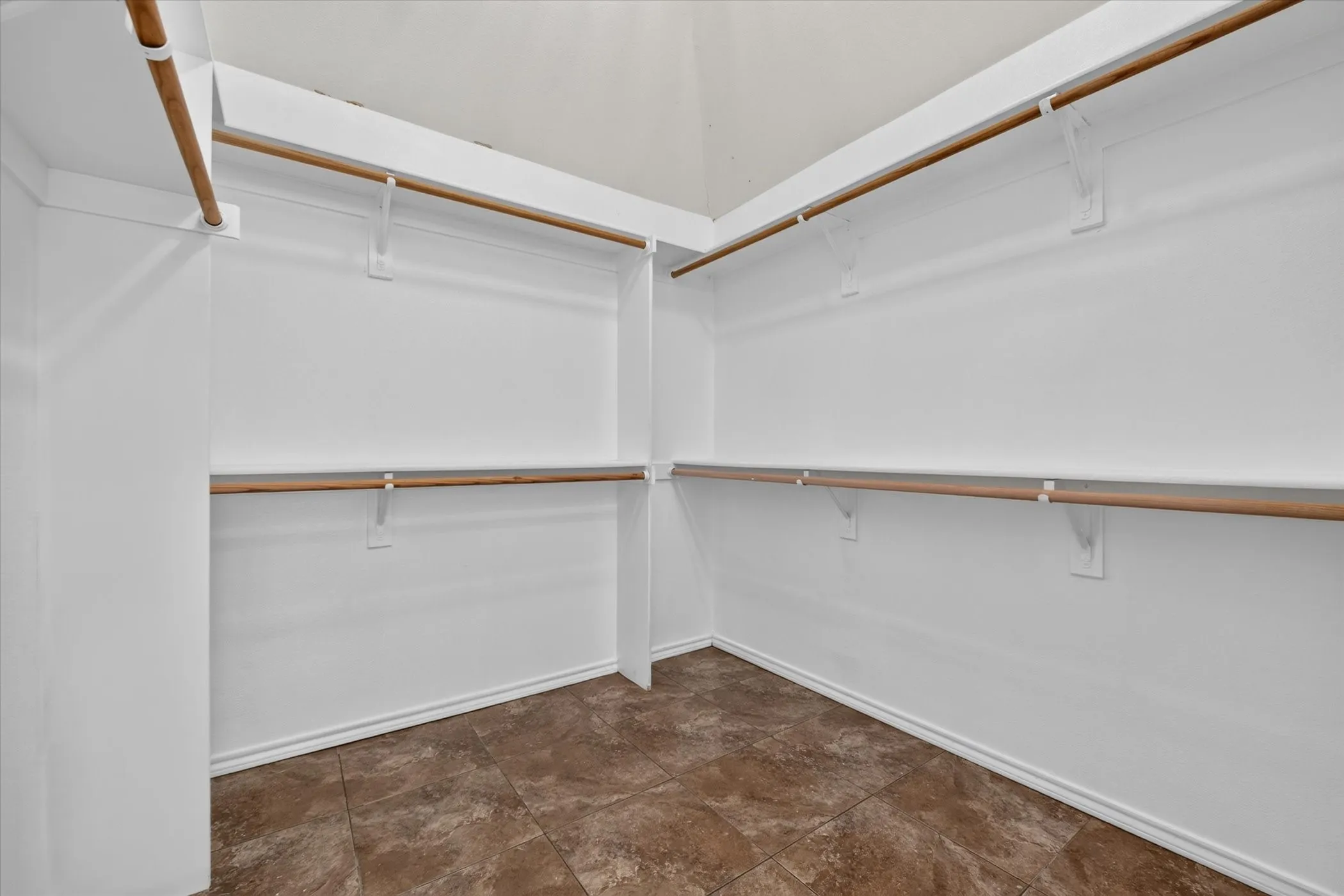 Expansive closet with multiple hanging rods, integrated shelving, and tile flooring