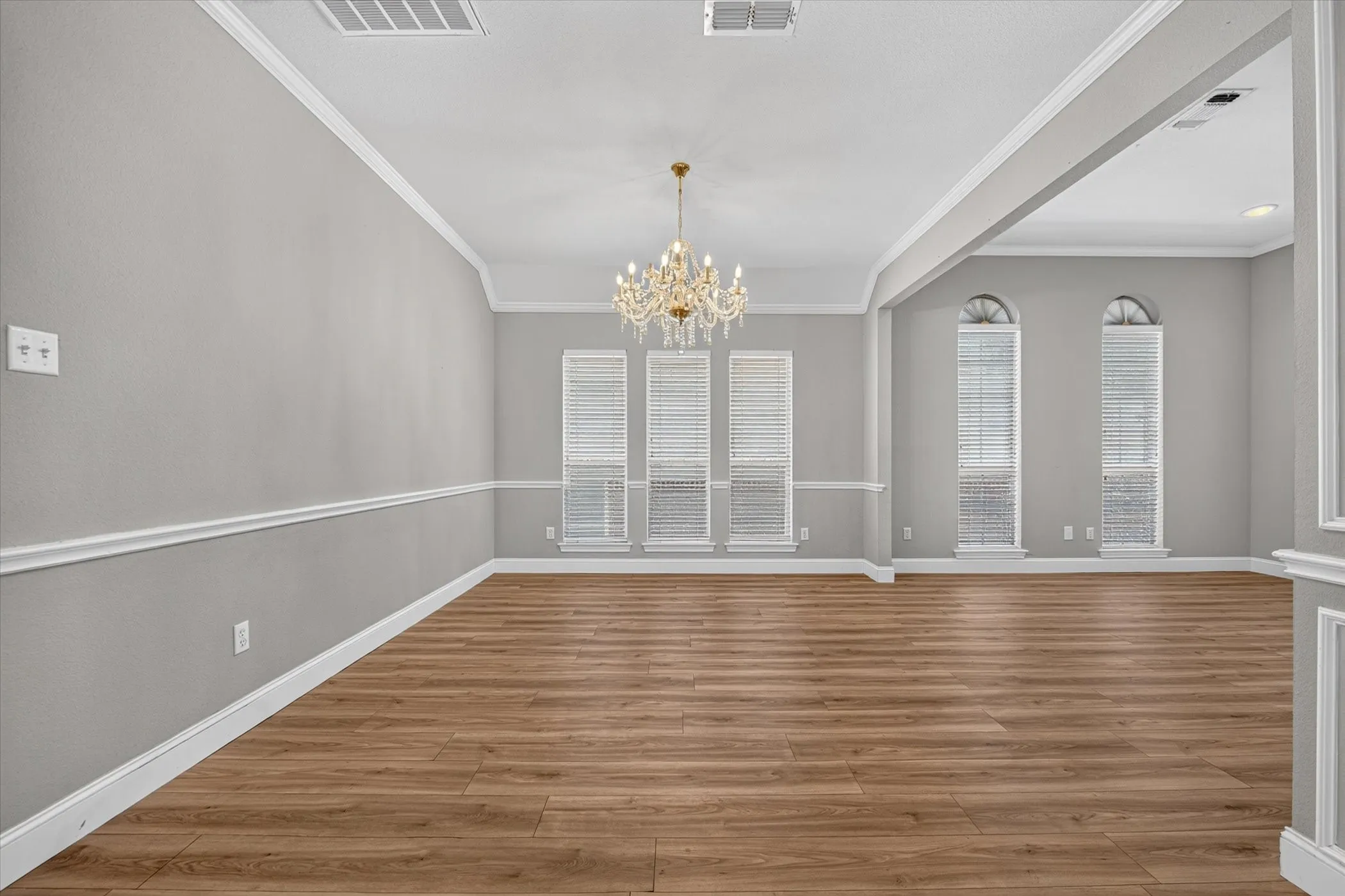 Wood-finish flooring, crown molding, chair rail molding, a crystal chandelier, and arched windows