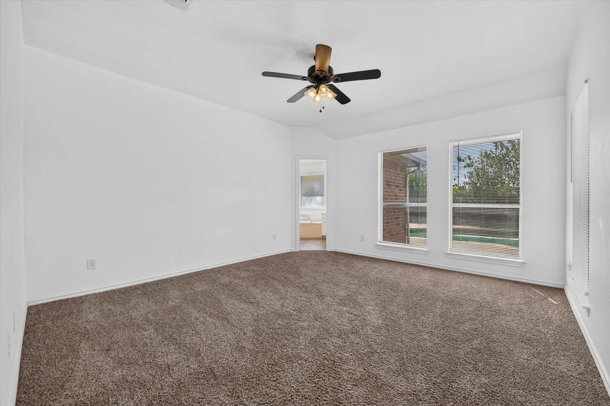 Spacious room featuring vaulted ceilings, two large windows, a ceiling fan with integrated lighting, and plush carpeting