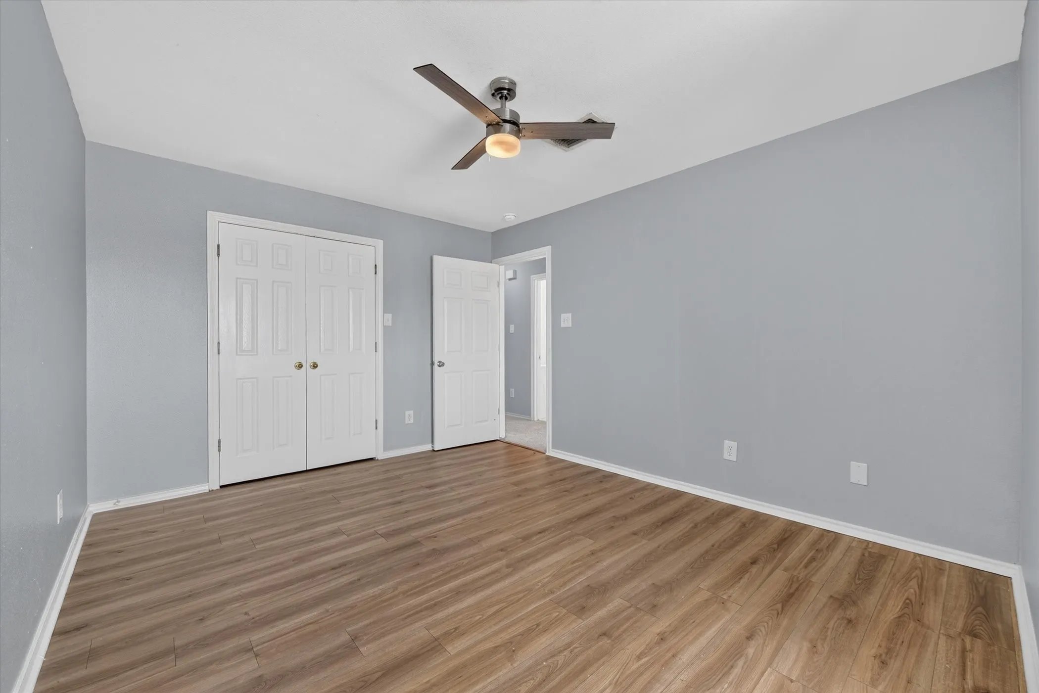 Wood-finish flooring, light gray wall paint, and a ceiling fan with integrated lighting