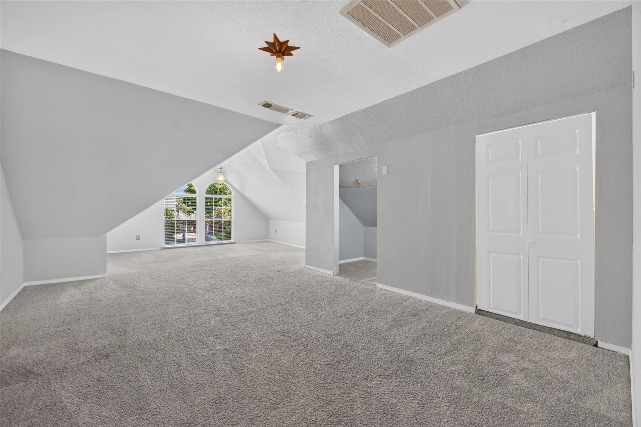 Spacious upper-level room featuring gray carpeting, sloped ceilings, and arched windows
