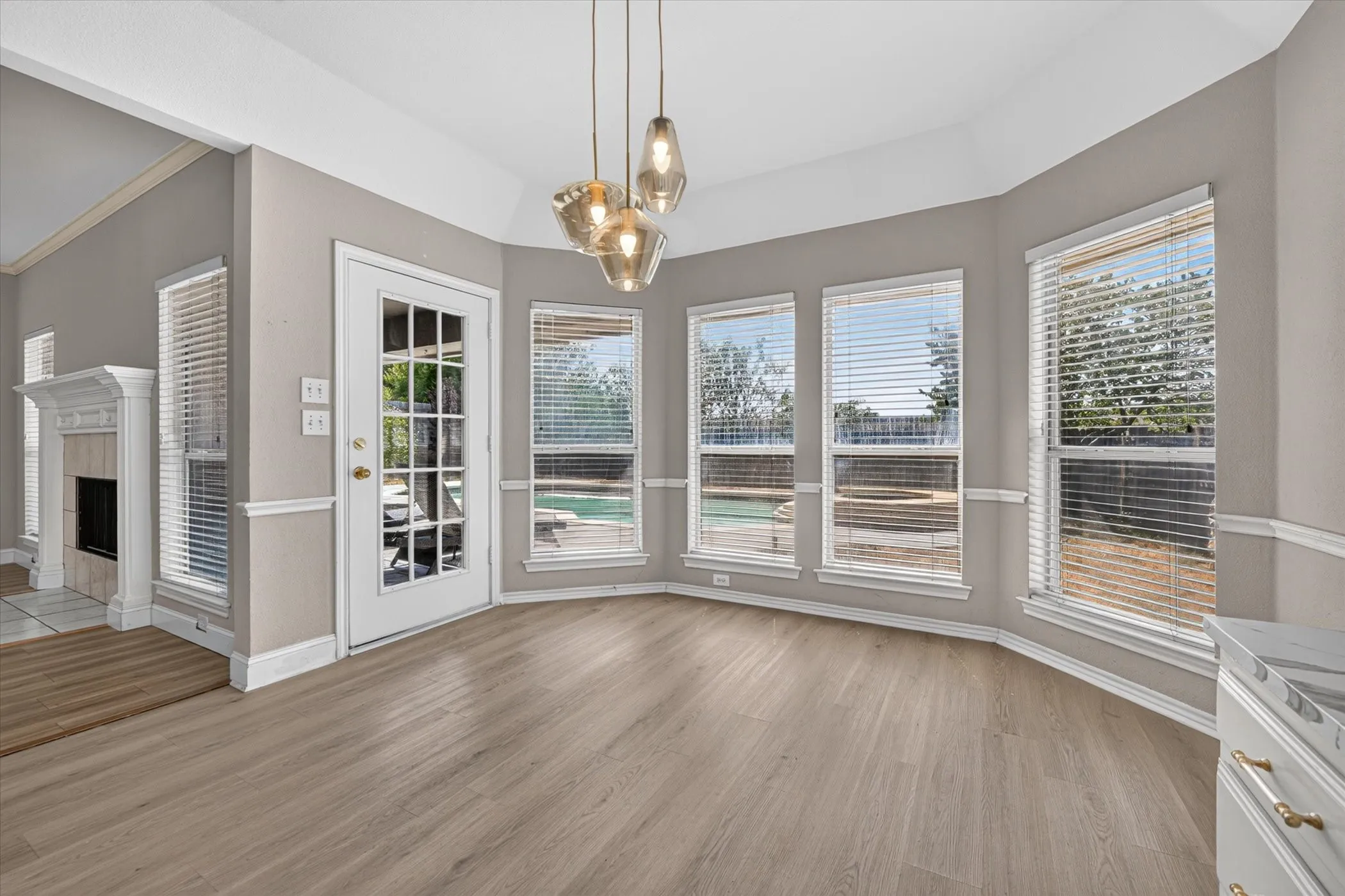 Bay window design, wood-finish flooring, French door with glass panels, three pendant light fixtures, and a corner fireplace with a white mantel
