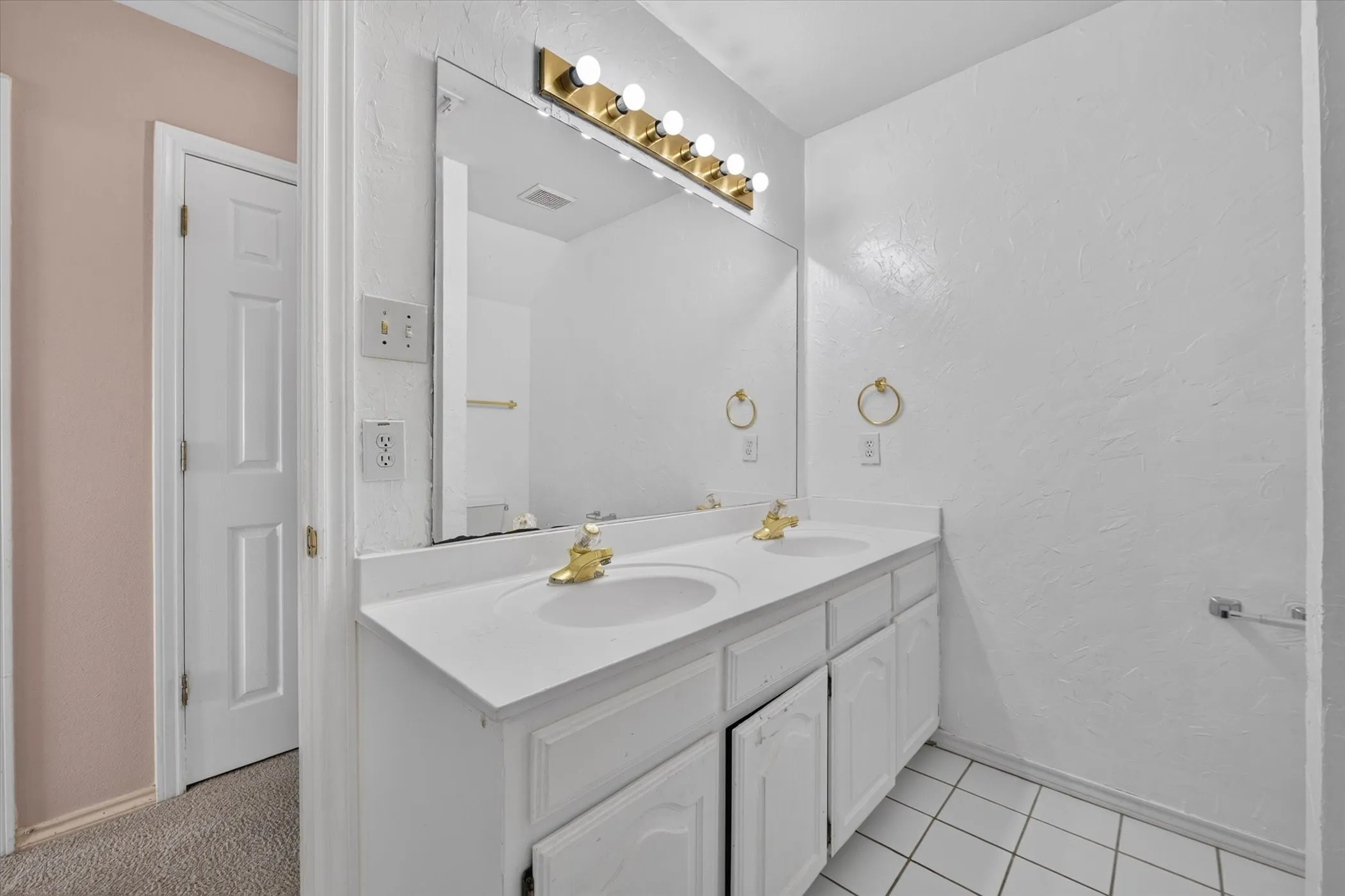 Dual vanity with integrated sinks, white cabinetry, gold-tone hardware, and a large wall-mounted mirror
