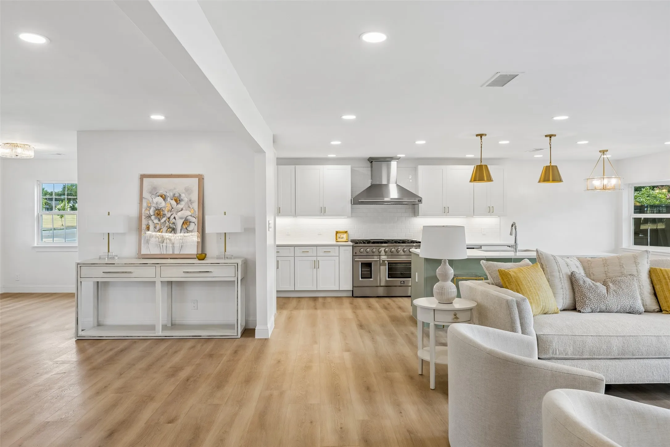 Sunlit living and kitchen area featuring a professional range with brushed gold pendants and sleek white cabinetry.