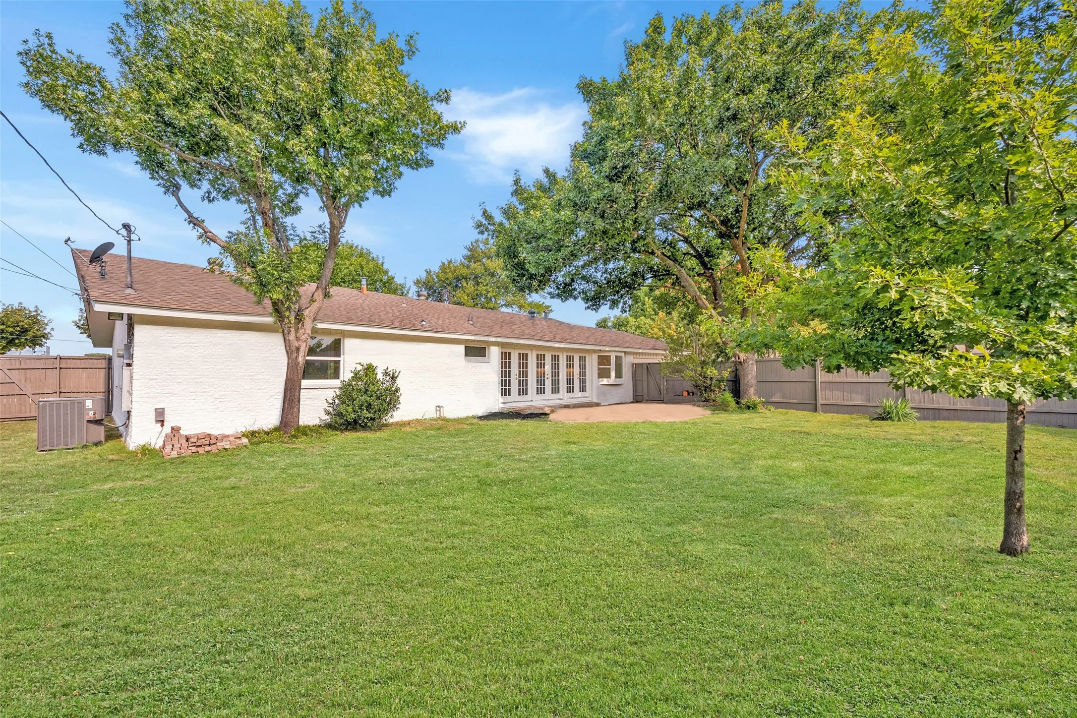Classic white brick ranch home with a sprawling green backyard, mature shade trees, and a French door entry onto the patio.