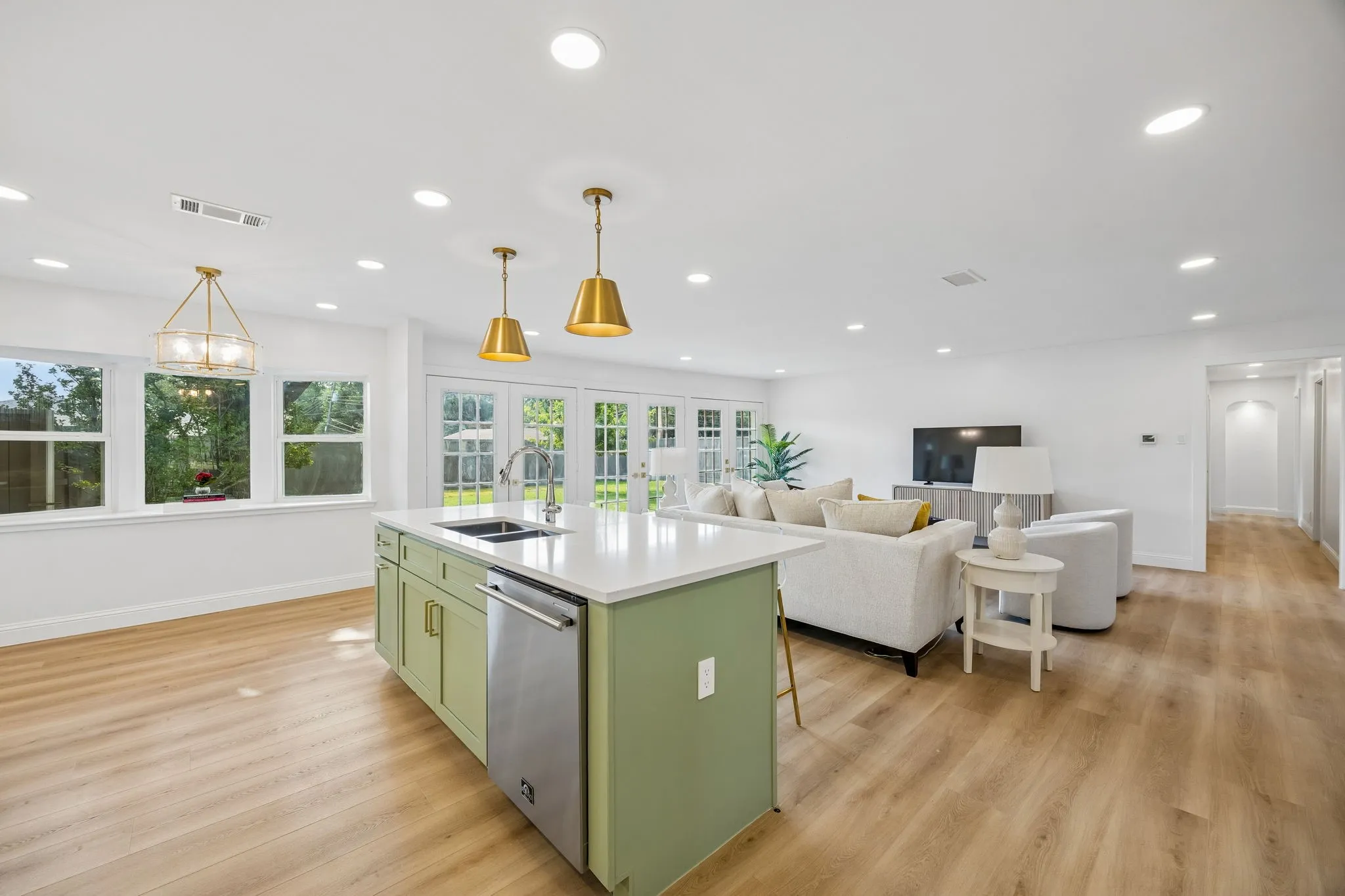Stylish kitchen island in sage green with quartz counters and brass pendants, opening directly into the adjoining living room.
