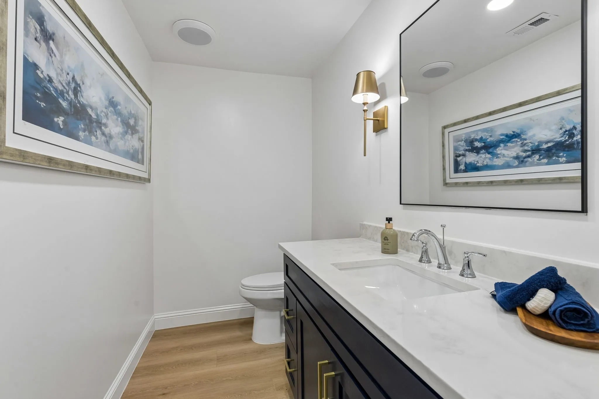 Elegant powder bath with navy vanity, brushed gold hardware and sconces, and a sleek quartz countertop for a refined finishing touch.