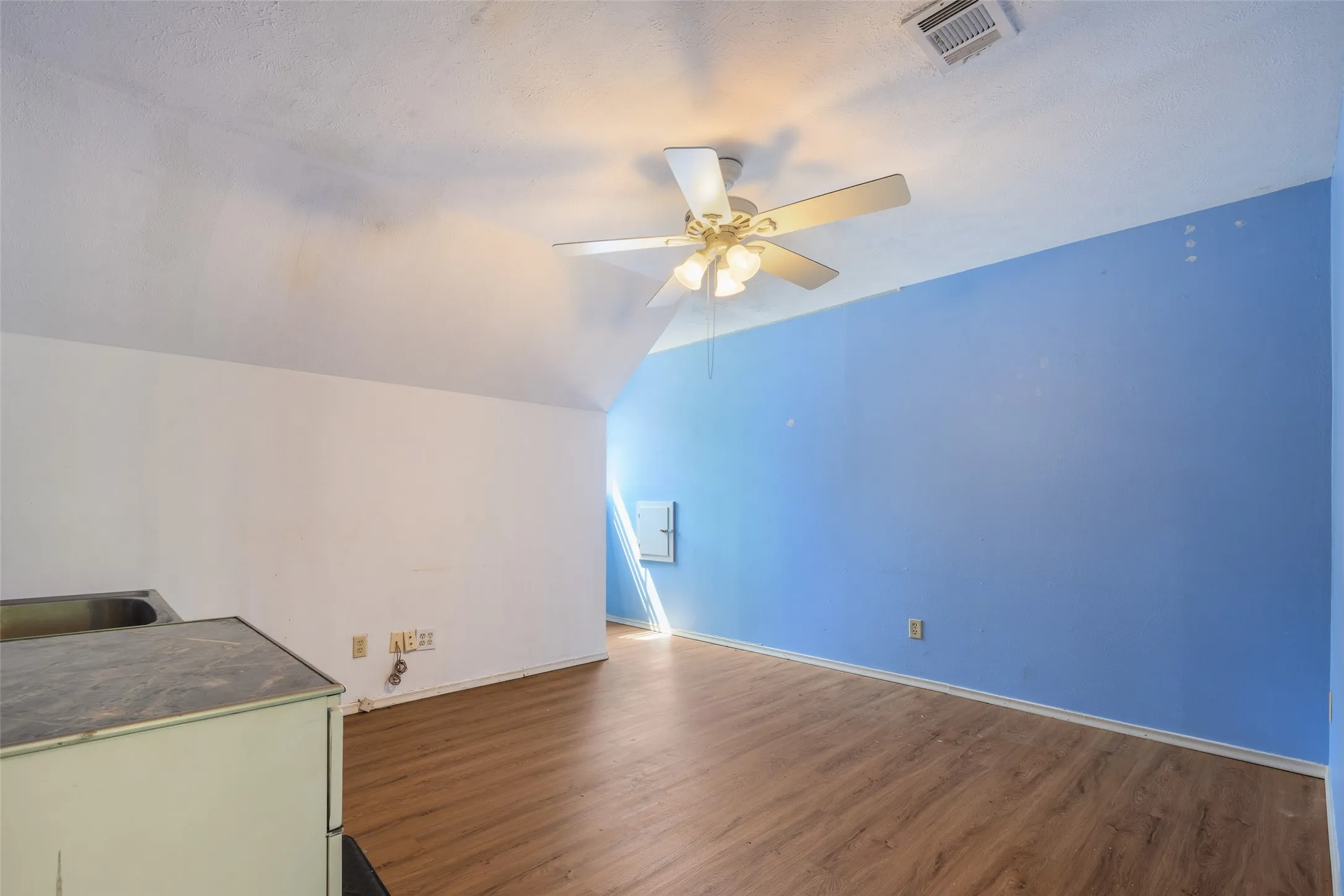 Sloped ceiling with an integrated ceiling fan, wood-finish flooring, and a compact utility sink