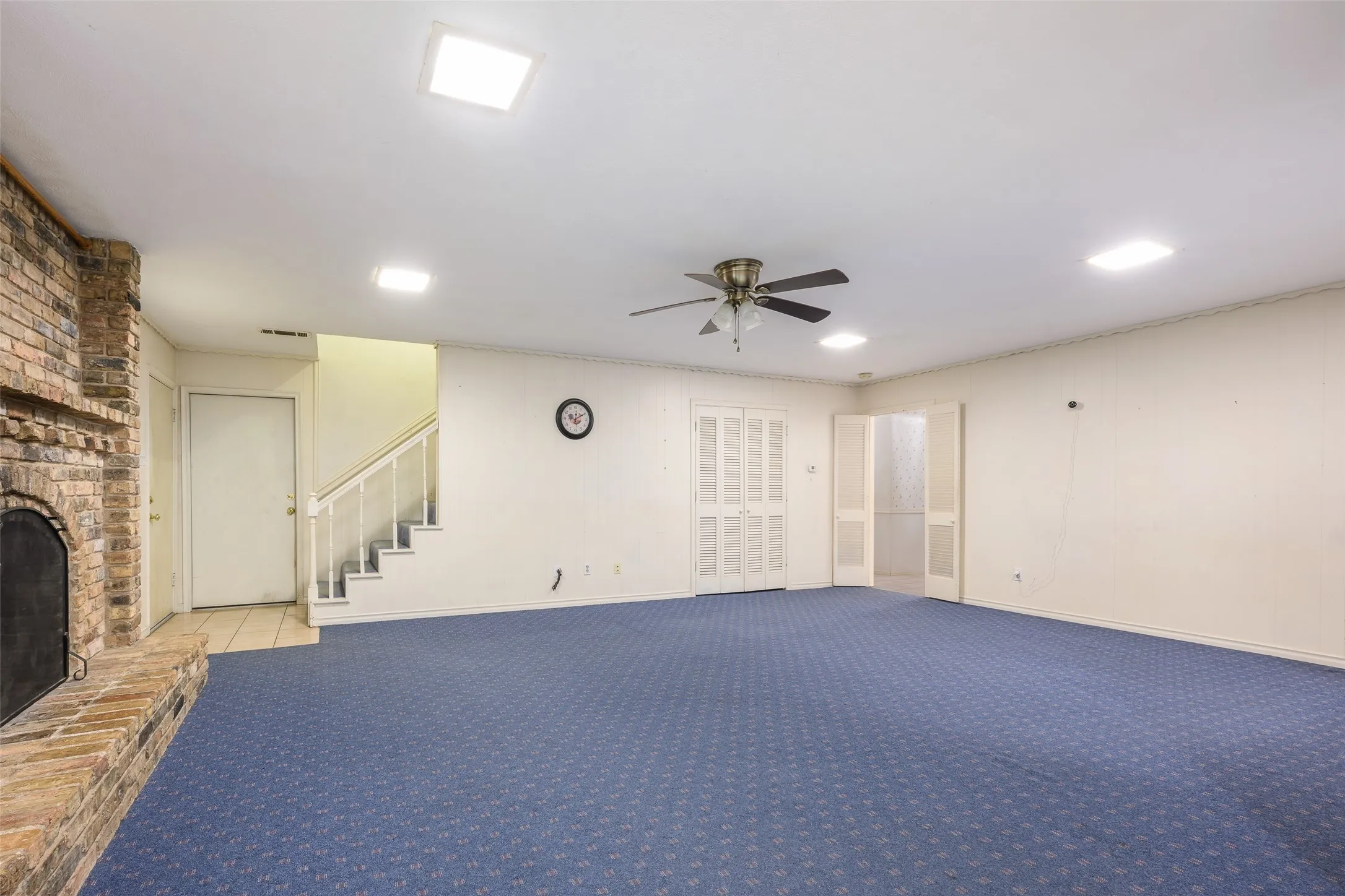 Exposed brick fireplace with a hearth, recessed ceiling lighting, a ceiling fan, and carpeted flooring