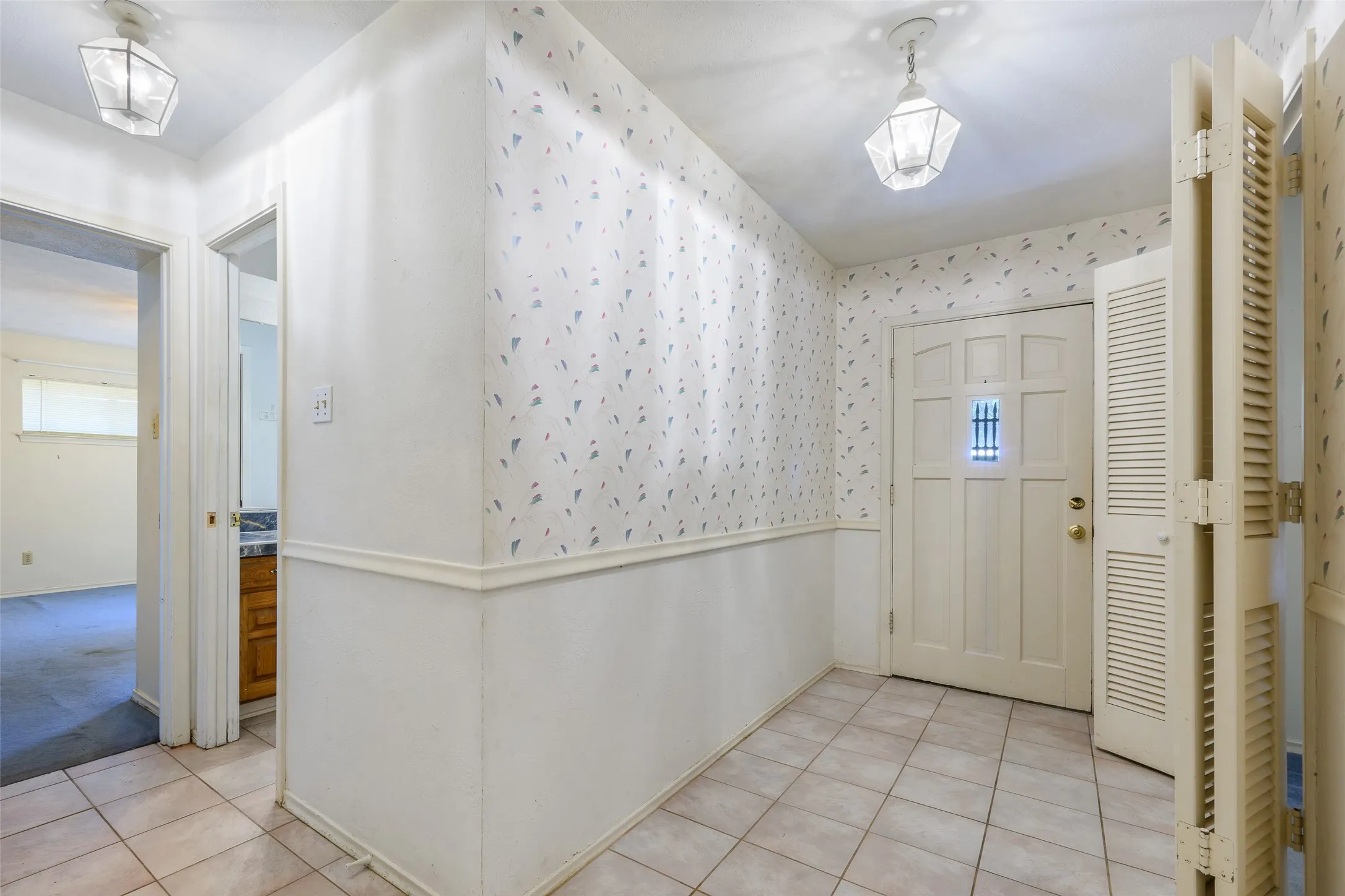 Tile flooring in the entry, decorative front door, and wall-mounted lighting fixtures