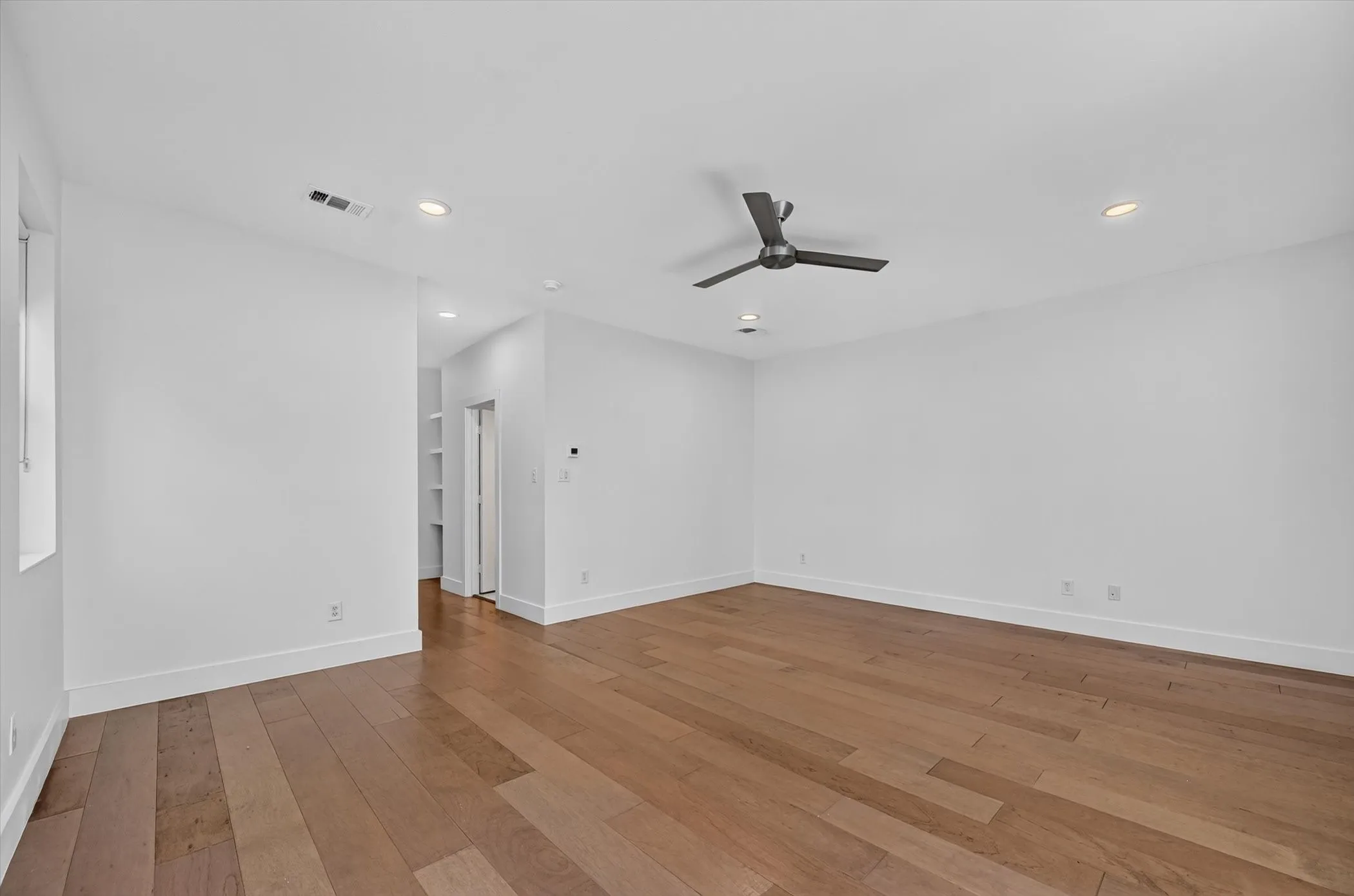 Spacious room featuring wood-finish flooring, recessed lighting, and a ceiling fan