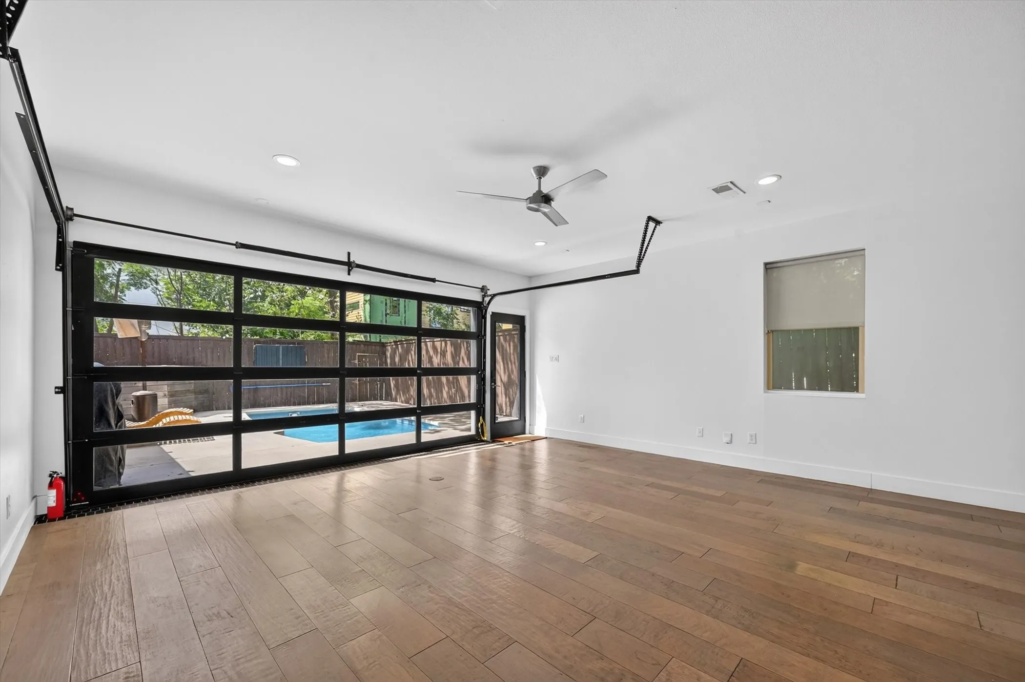 Wood-finish flooring throughout, full-length glass roll-up door, recessed lighting, and a ceiling fan