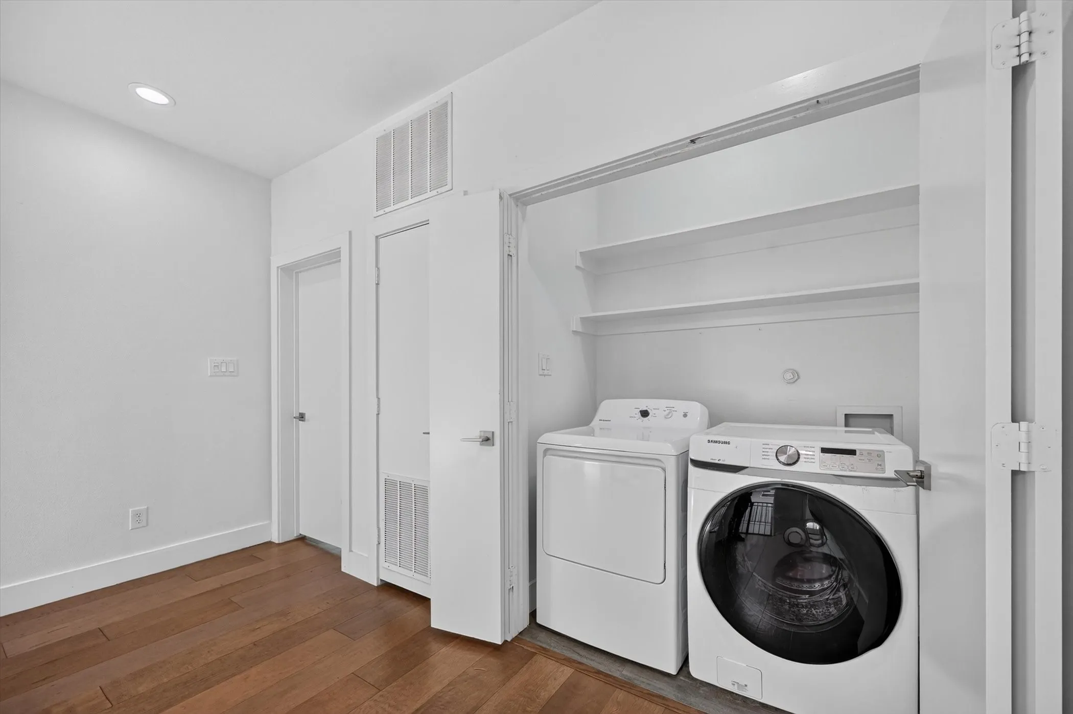In-unit laundry closet with built-in shelving, front-load washer, and top-load dryer