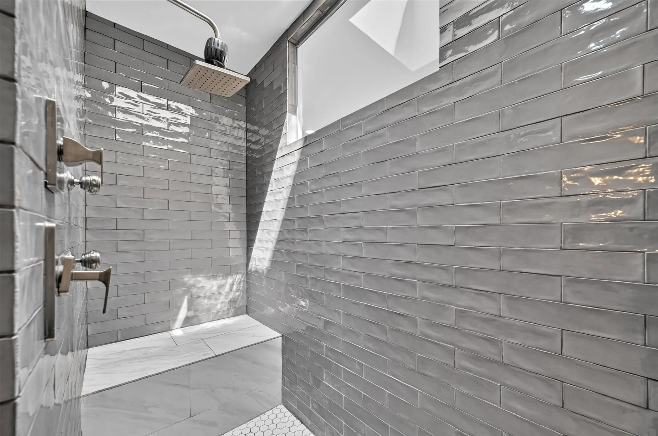Shower enclosure featuring gray subway tile, a fixed rainfall shower head, and a built-in bench