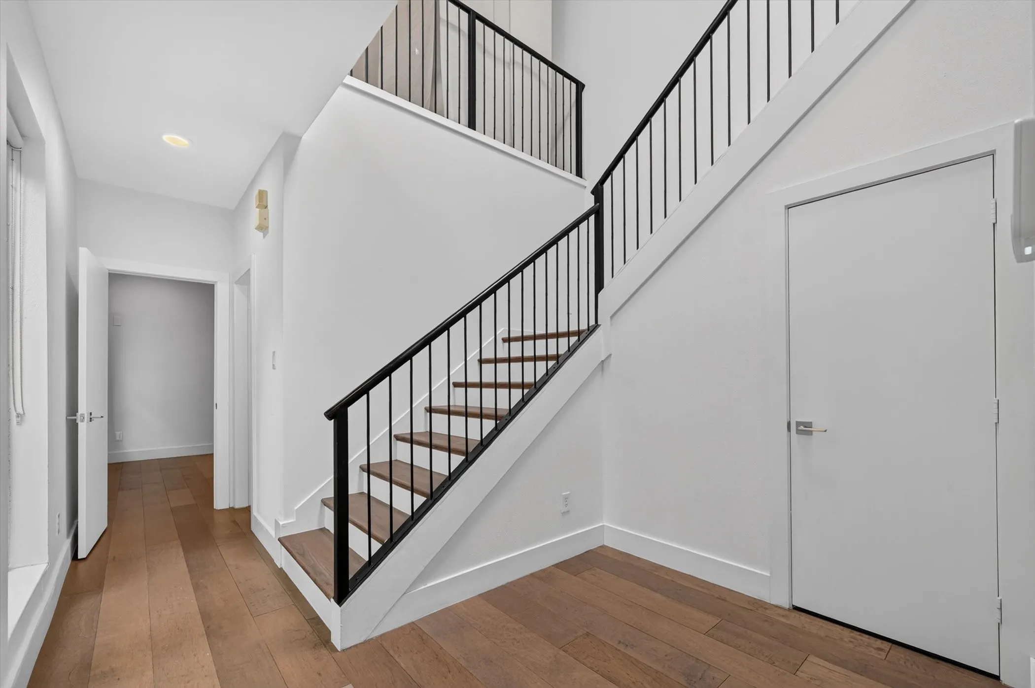 Hardwood flooring throughout, modern staircase with black metal balusters, recessed lighting, and white walls
