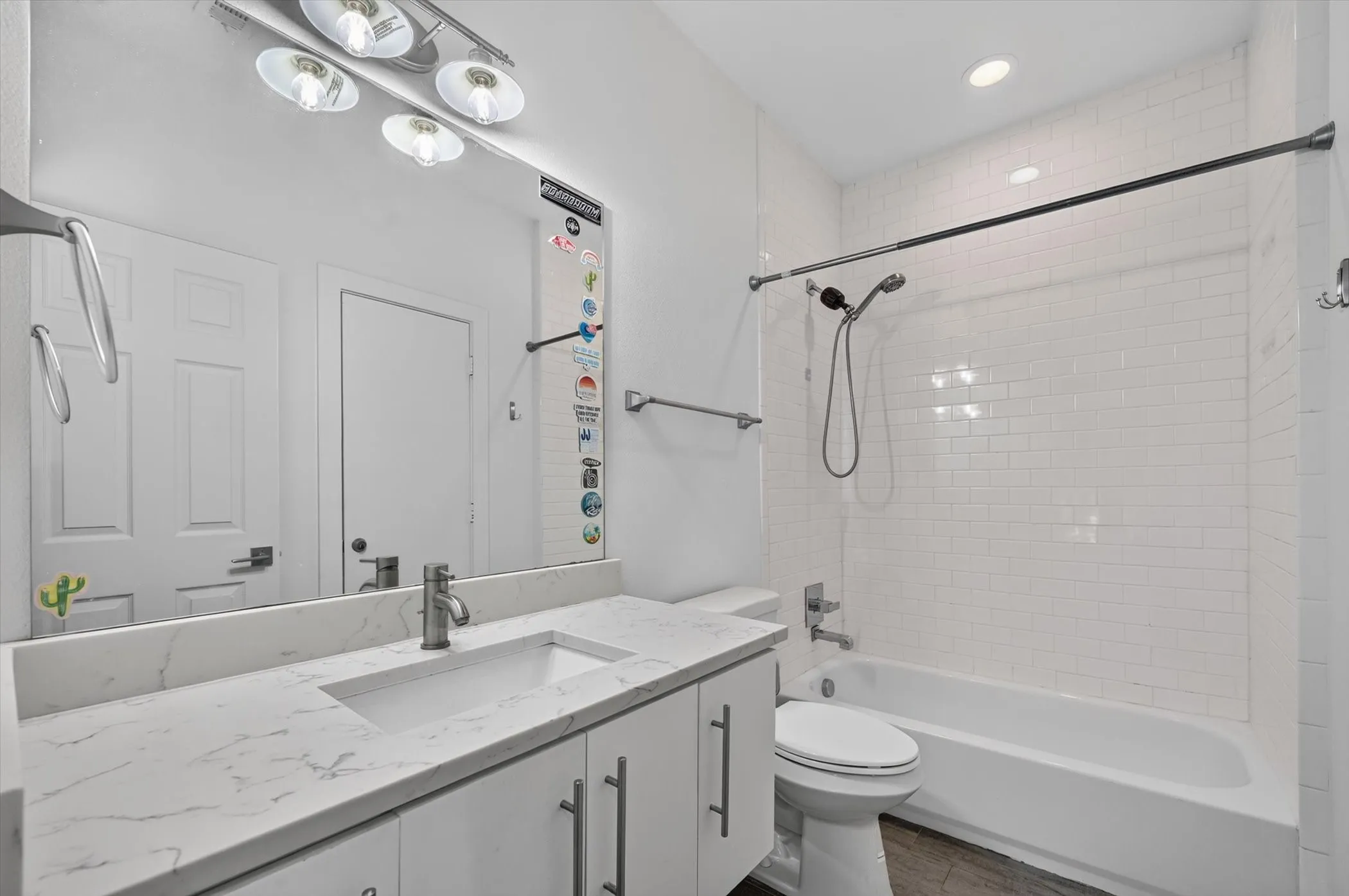 White subway tile shower surround with a built-in tub, a single vanity with a white countertop, and a large wall-mounted mirror