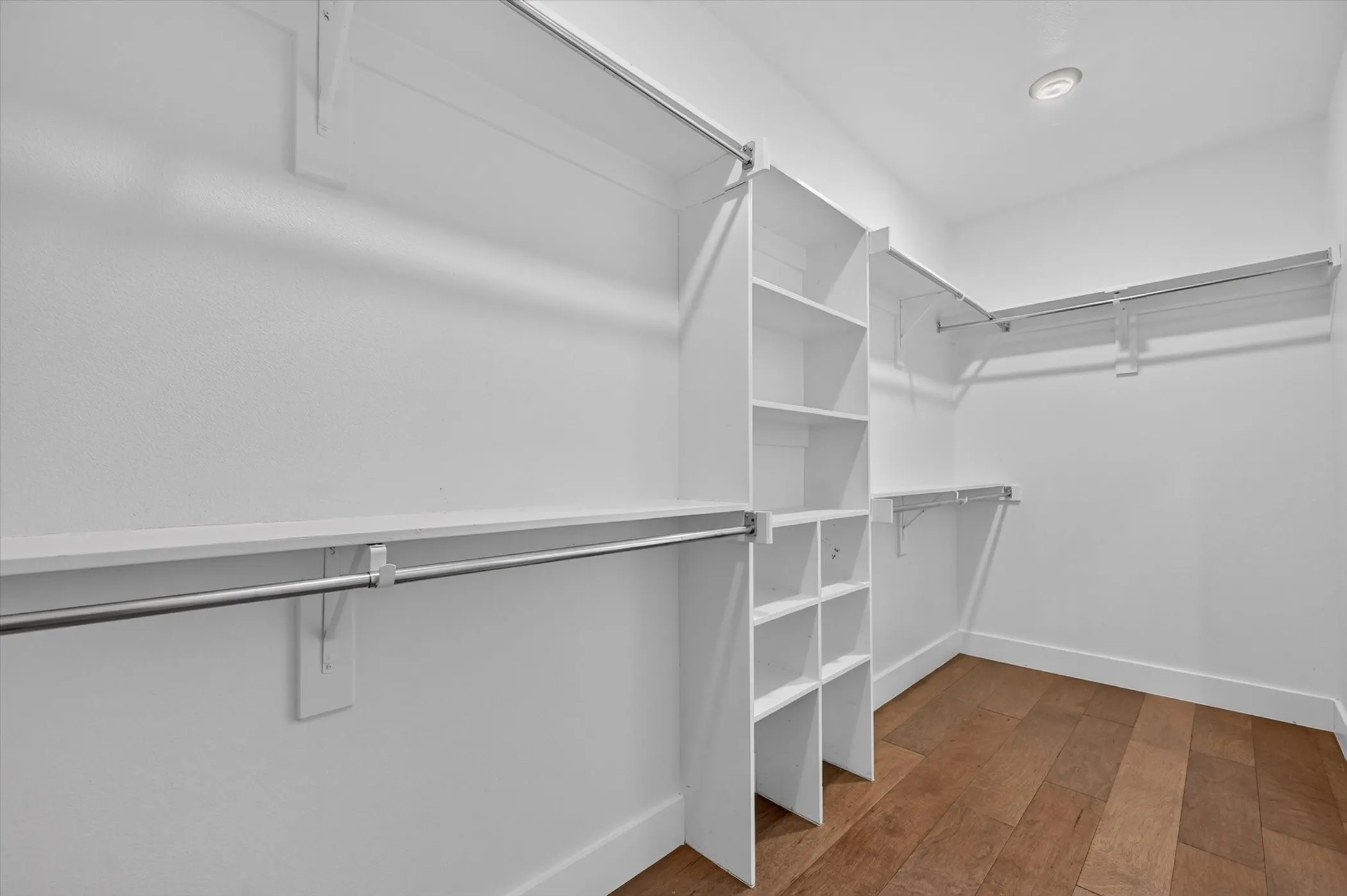Walk-in closet with integrated shelving, multiple hanging rods, and wood-finish flooring