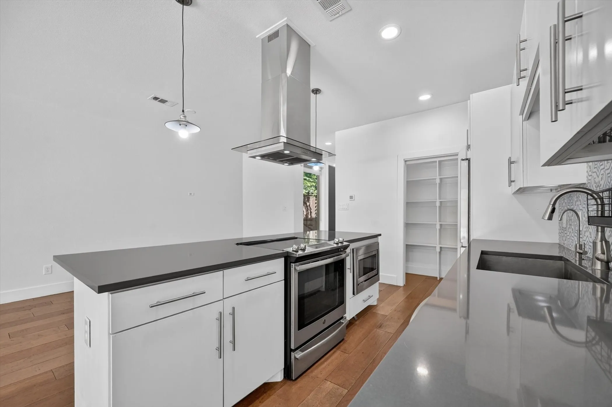 Kitchen featuring an island with built-in range, stainless steel appliances, pendant lighting, and a walk-in pantry