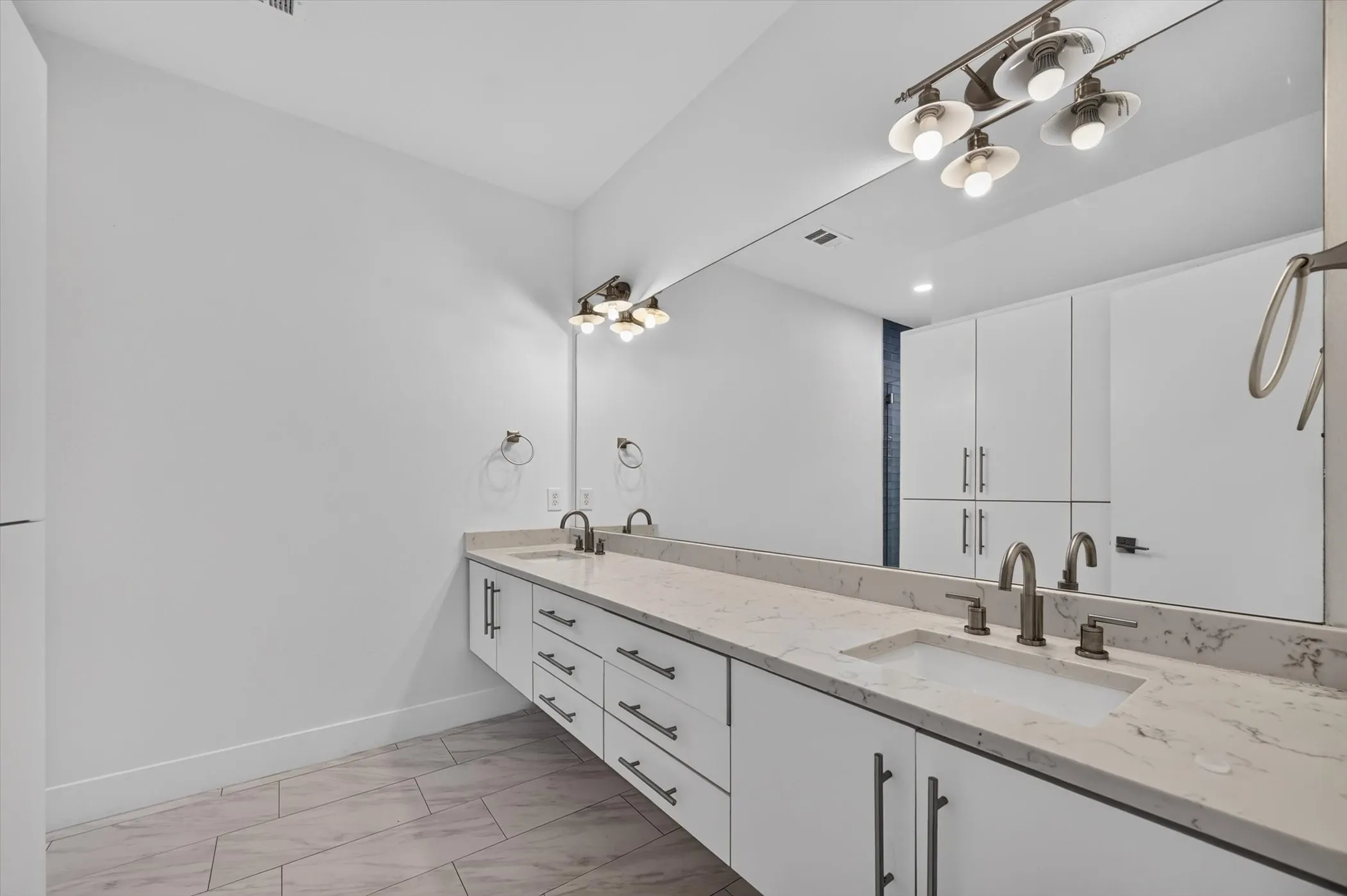 Spa-inspired primary bathroom featuring a lengthy dual-sink vanity with white cabinetry, light wood-finish countertops, and brushed nickel hardware