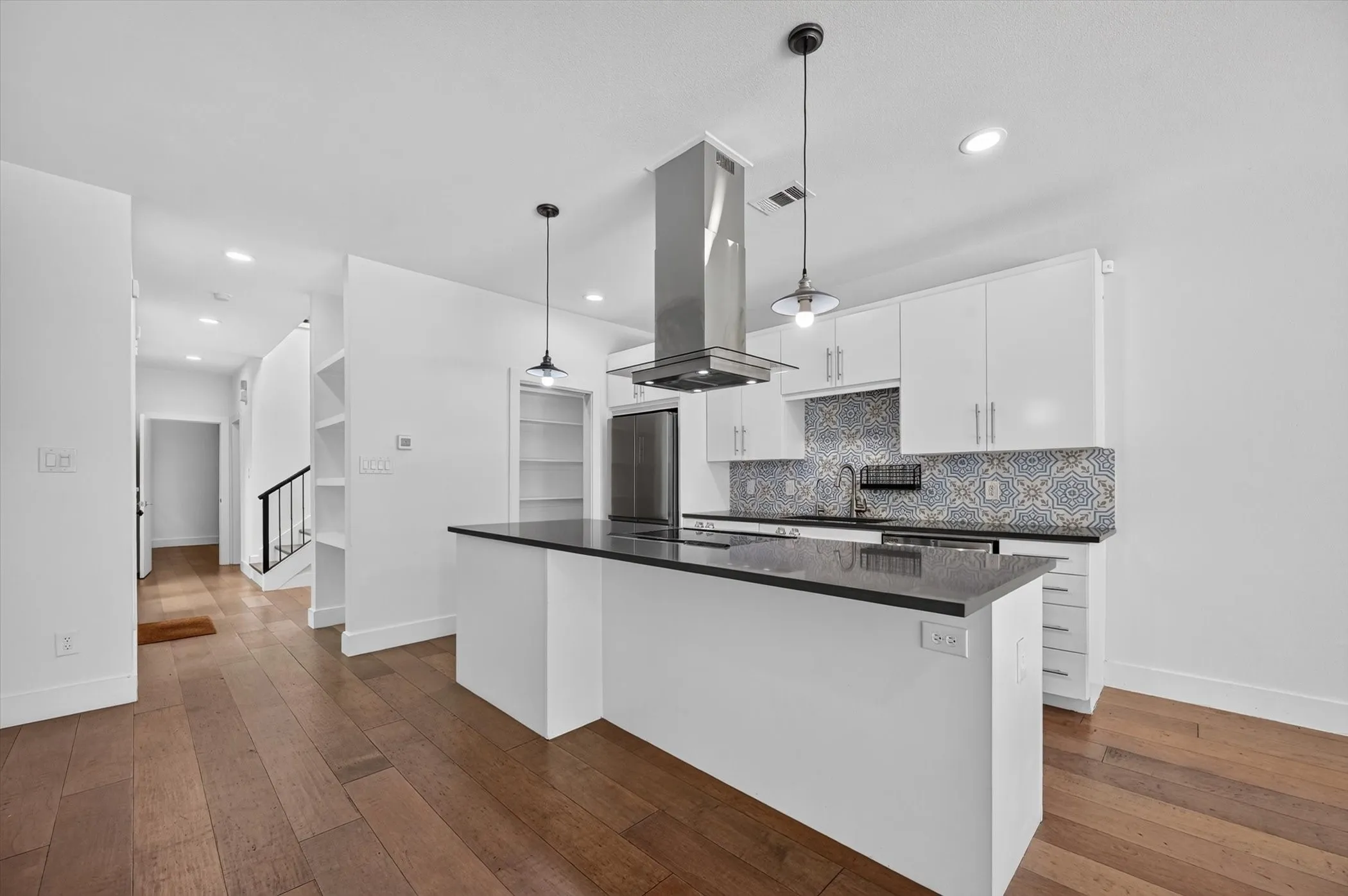 Kitchen featuring a center island with dark countertop, white cabinetry, patterned tile backsplash, and wood-finish flooring