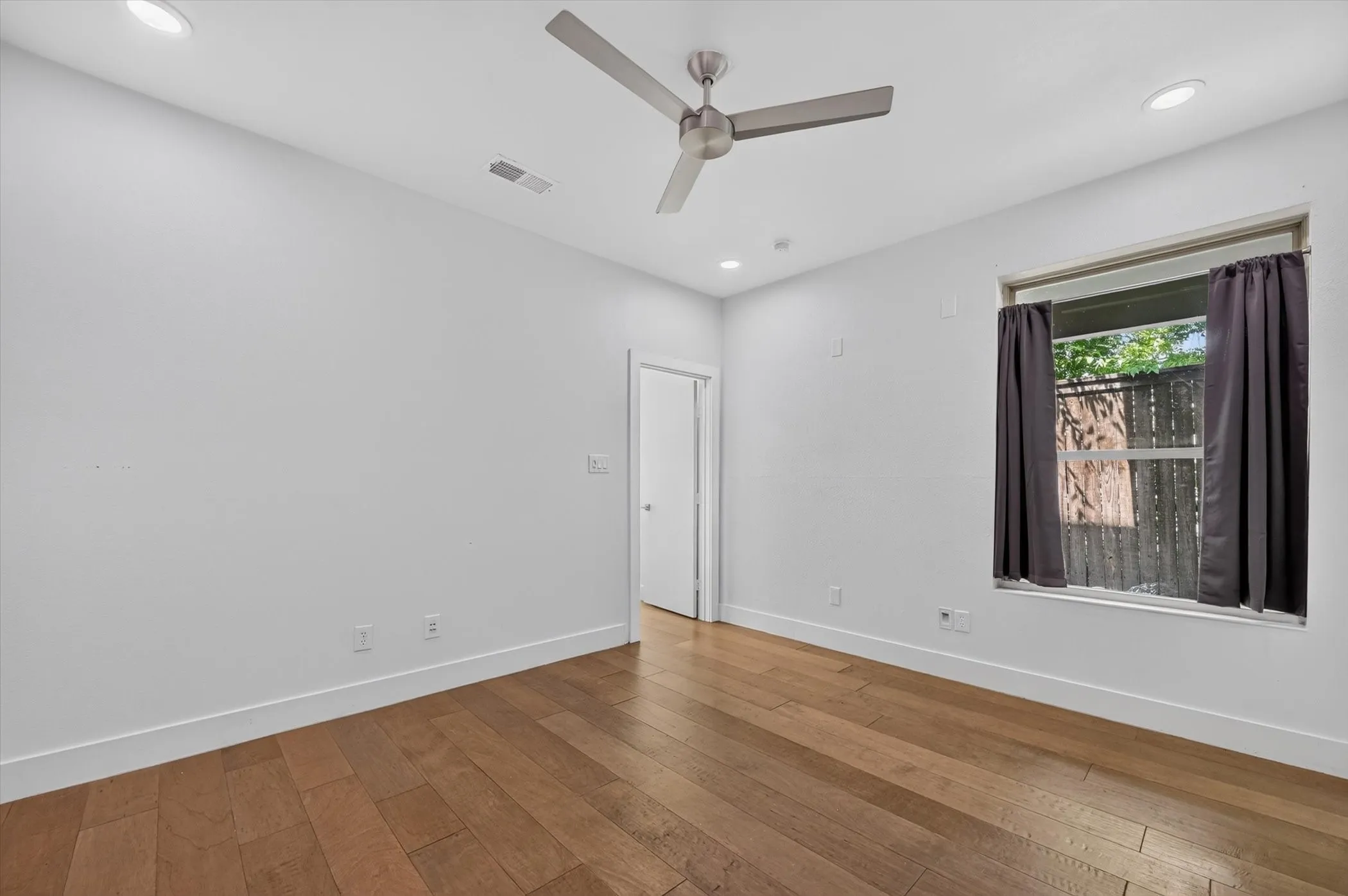 Hardwood flooring, recessed lighting, modern ceiling fan, white walls, and a window with natural light
