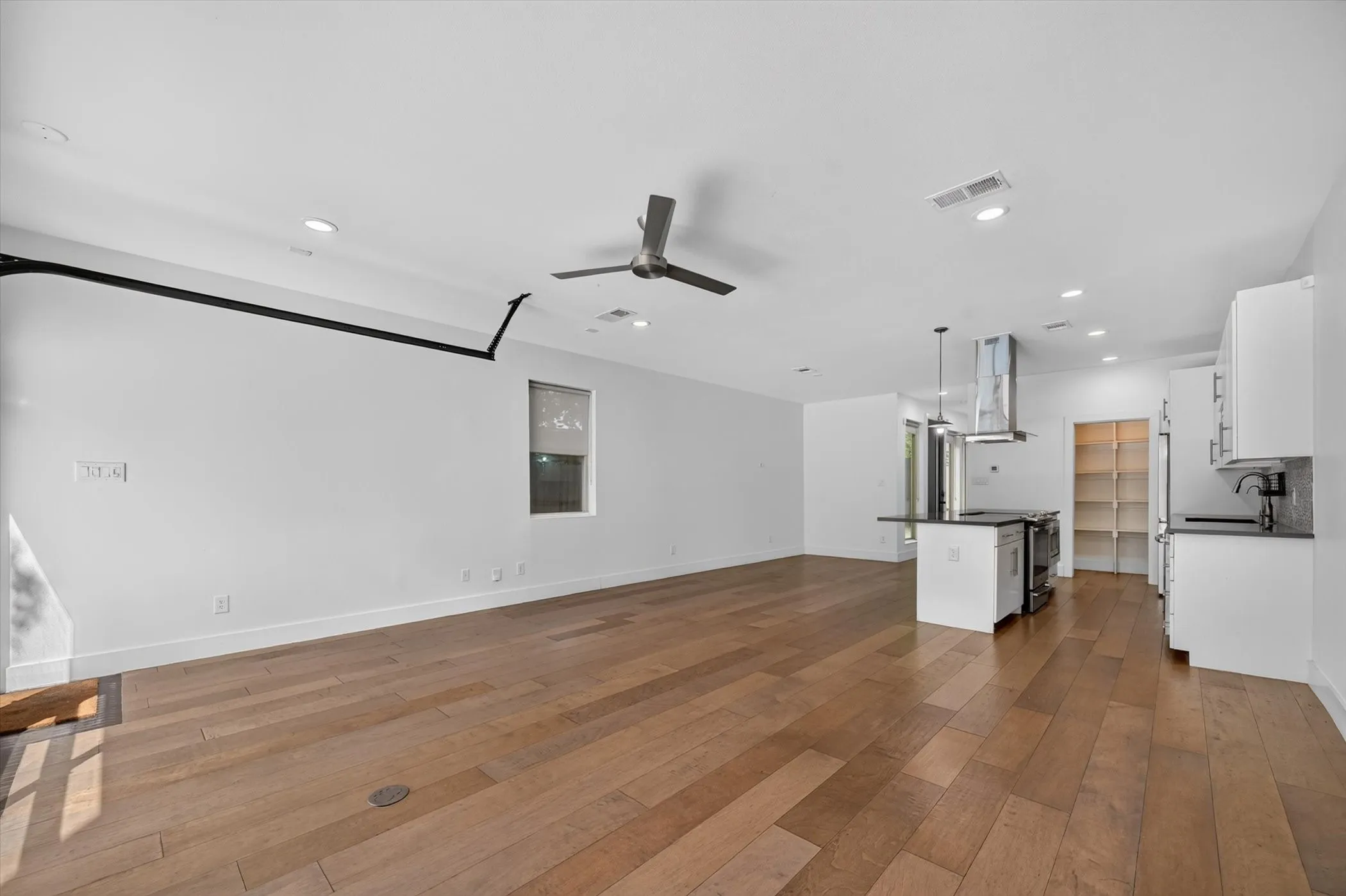 Open-concept living space with wood-finish flooring, recessed lighting, ceiling fan, kitchen island with pendant lighting, and stainless steel range hood