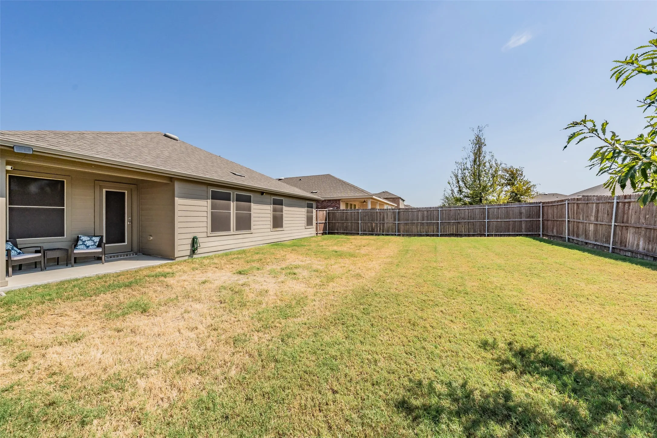 Expansive backyard with a wood privacy fence, concrete patio, and a covered back porch