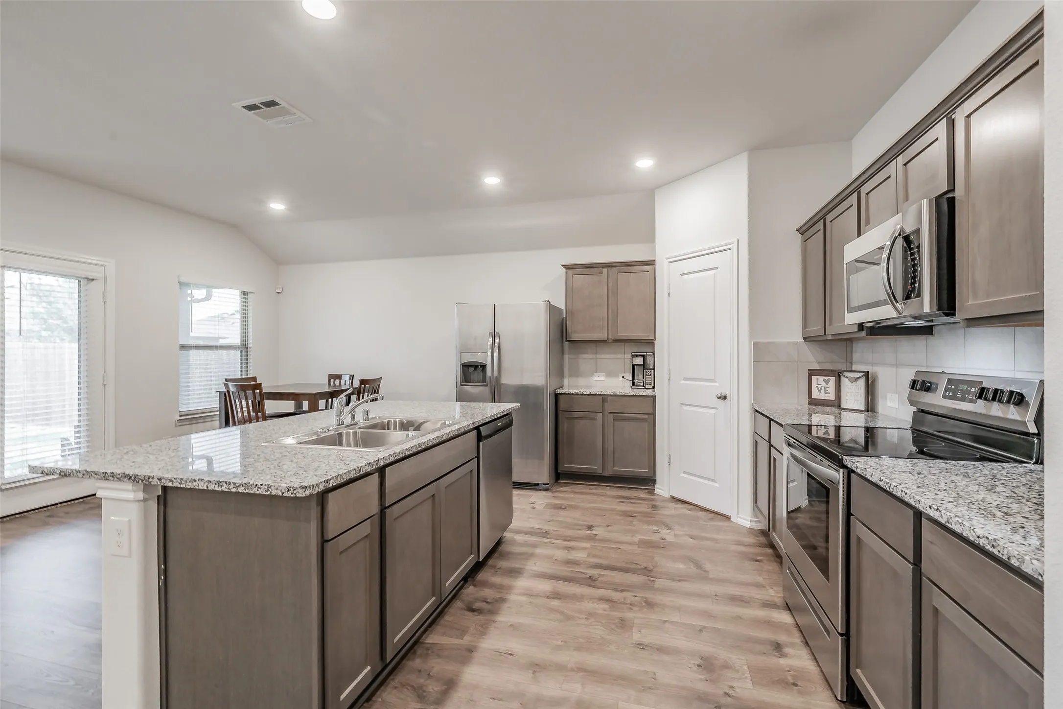 Kitchen featuring a center island with double basin sink, granite countertops, wood-finish flooring, stainless steel appliances, and recessed lighting
